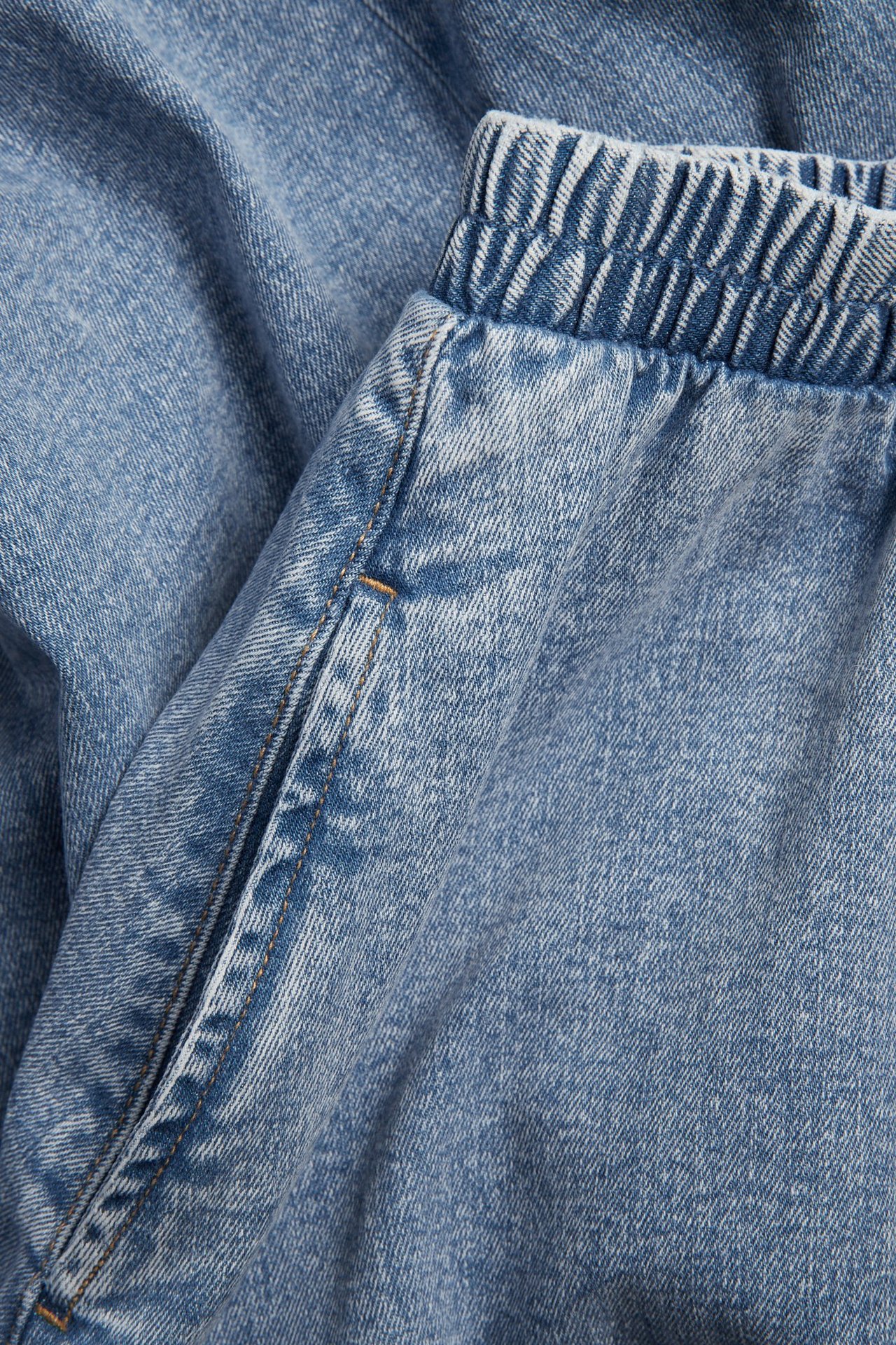 Nærbilde av et lys blått denim midiskjørt med strikk i livet og sidelomme.