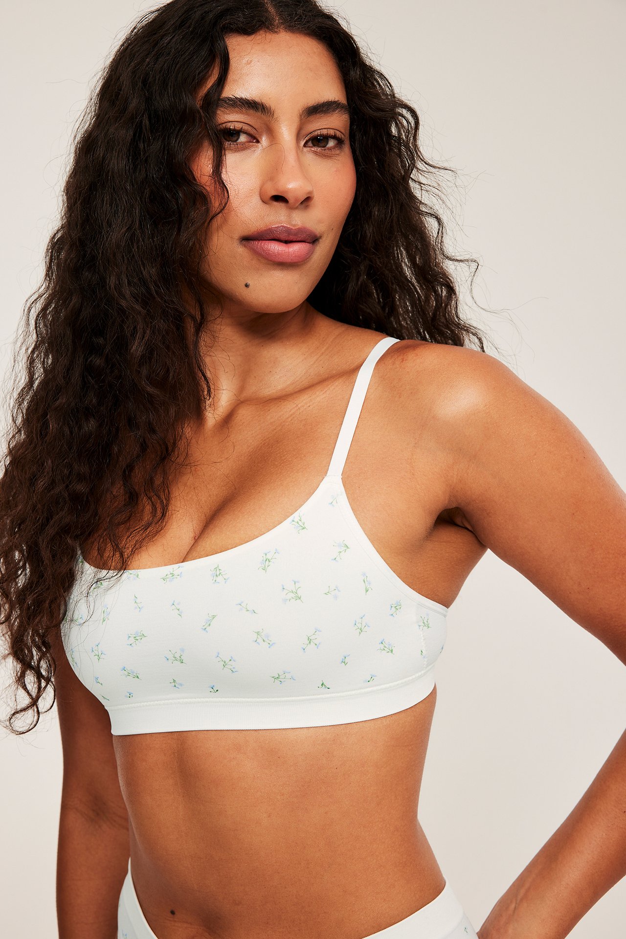 Widok z przodu kobiety w białym, bezszwowym biustonoszu z delikatnym niebiesko-zielonym wzorem kwiatowym.