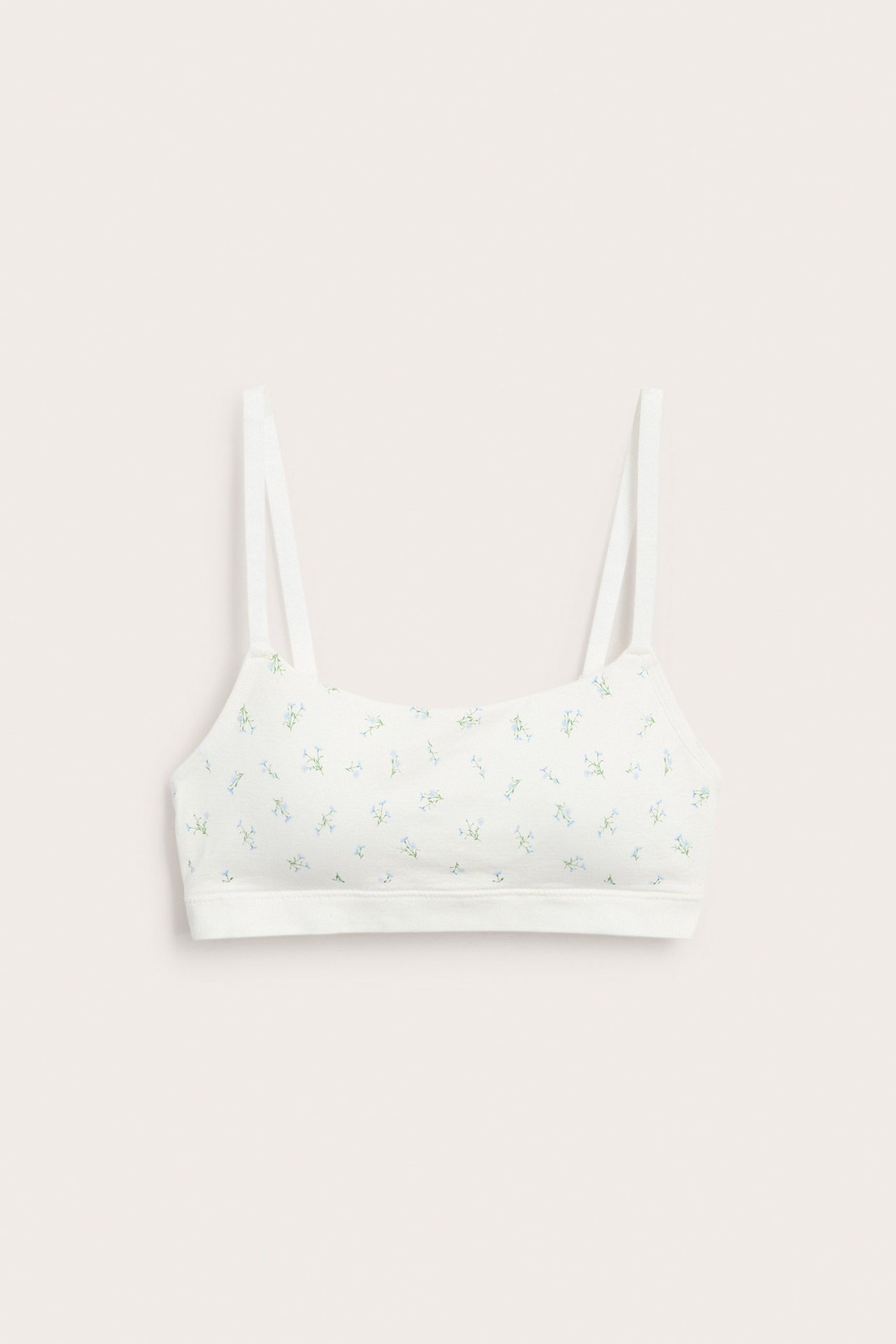 Edestäpäin, valkoinen saumaton bralette ohuilla olkaimilla ja herkällä sinisellä kukkakuviolla.