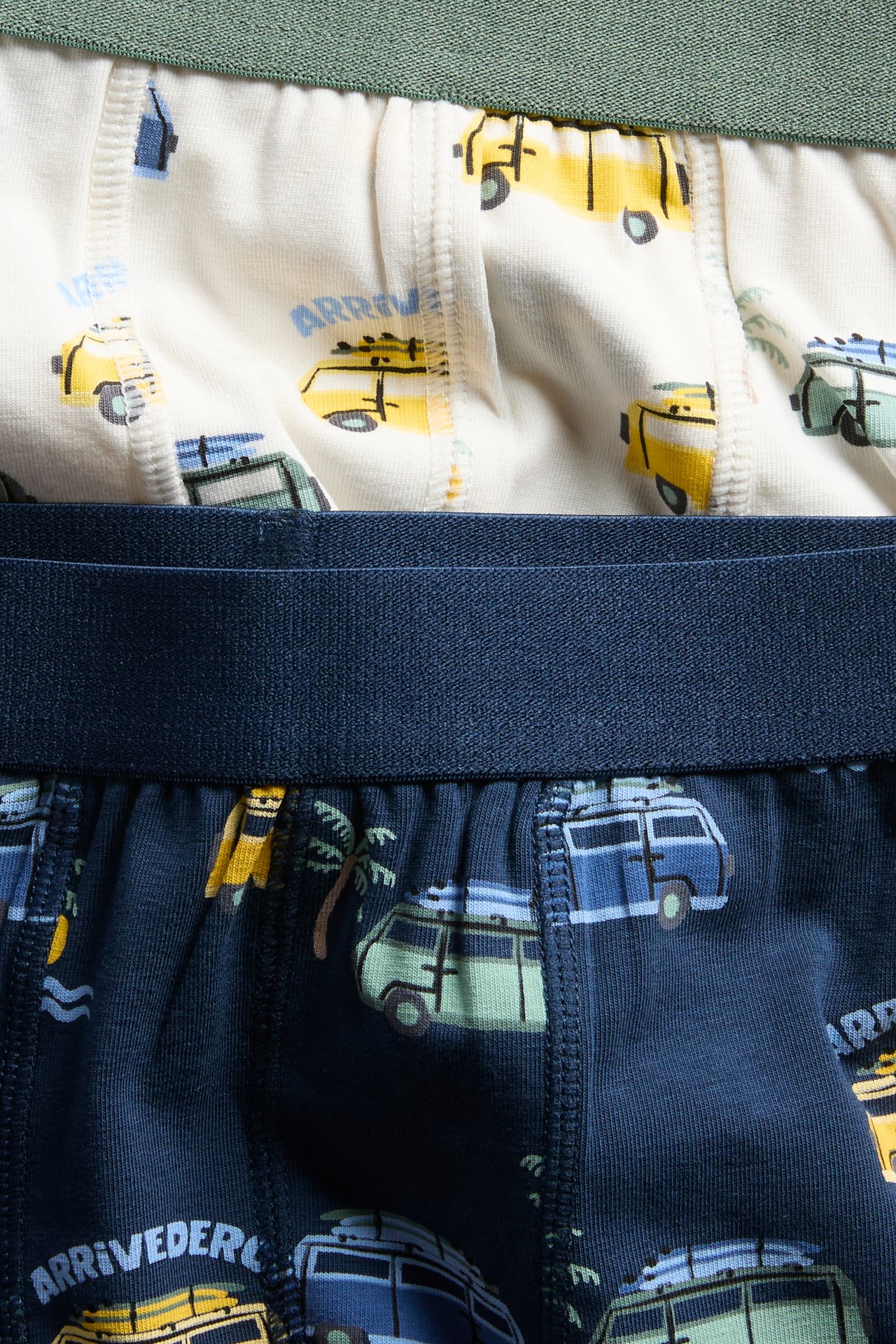 Närbild av mörkblå mönstrade barnboxershorts med fordon och benvita mönstrade boxershorts med fordon.