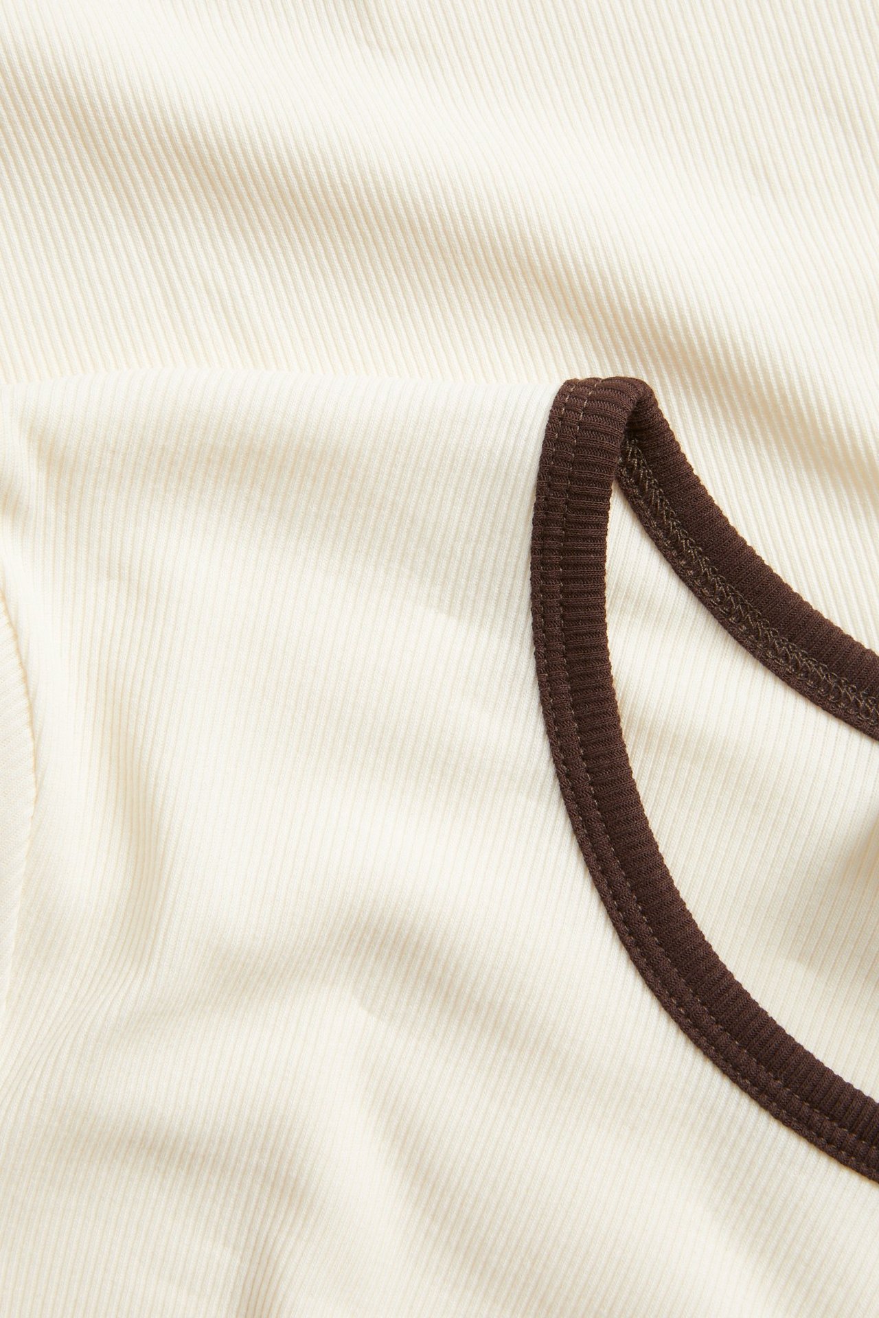 Lähikuva luonnonvalkoisesta ribatusta lyhythihaisesta topista, jossa on tummanruskeat kontrastireunat.