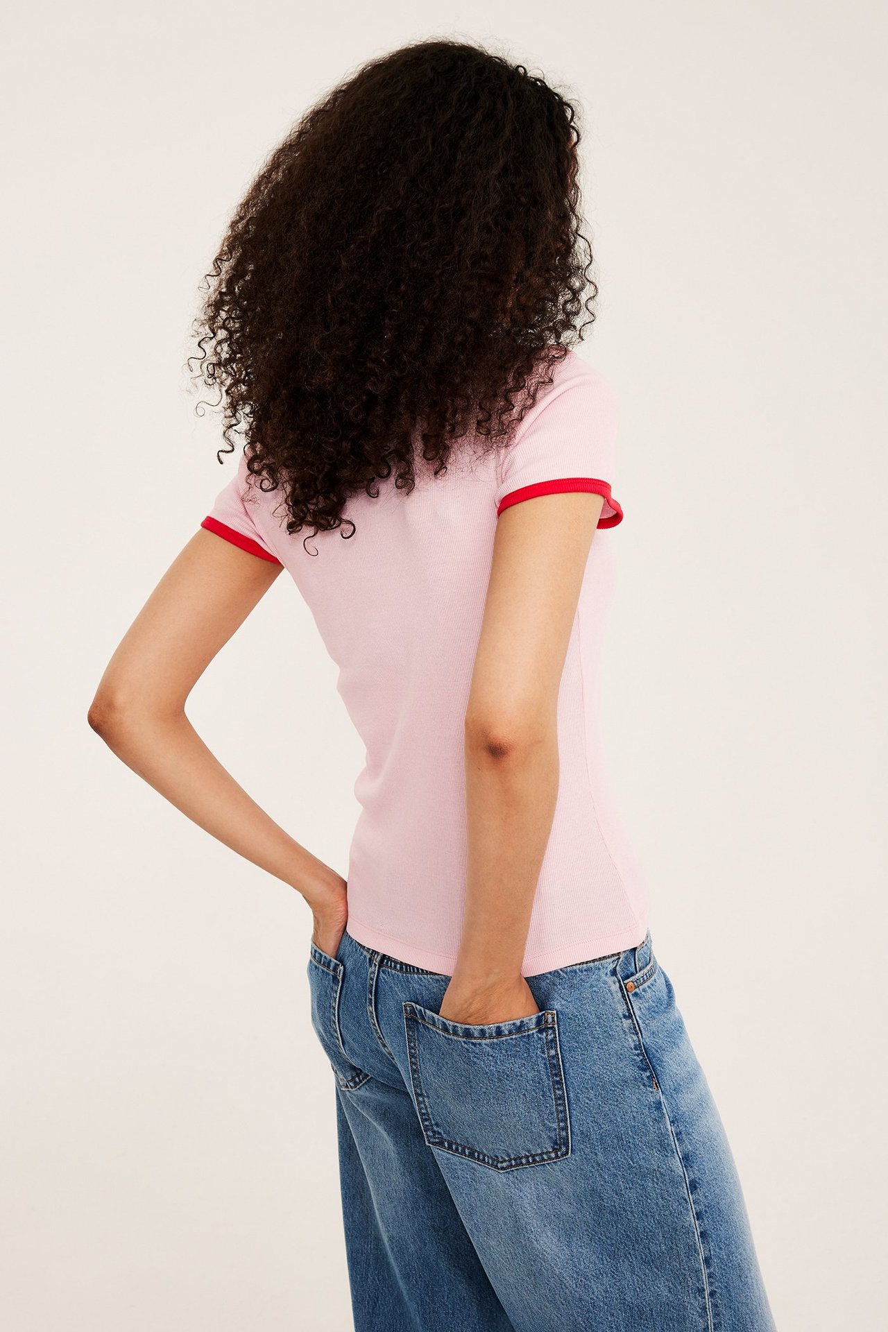 Naisen selkä, yllään vaaleanpunainen ribattu lyhythihainen toppi punaisilla kontrastireunoilla ja siniset farkut.