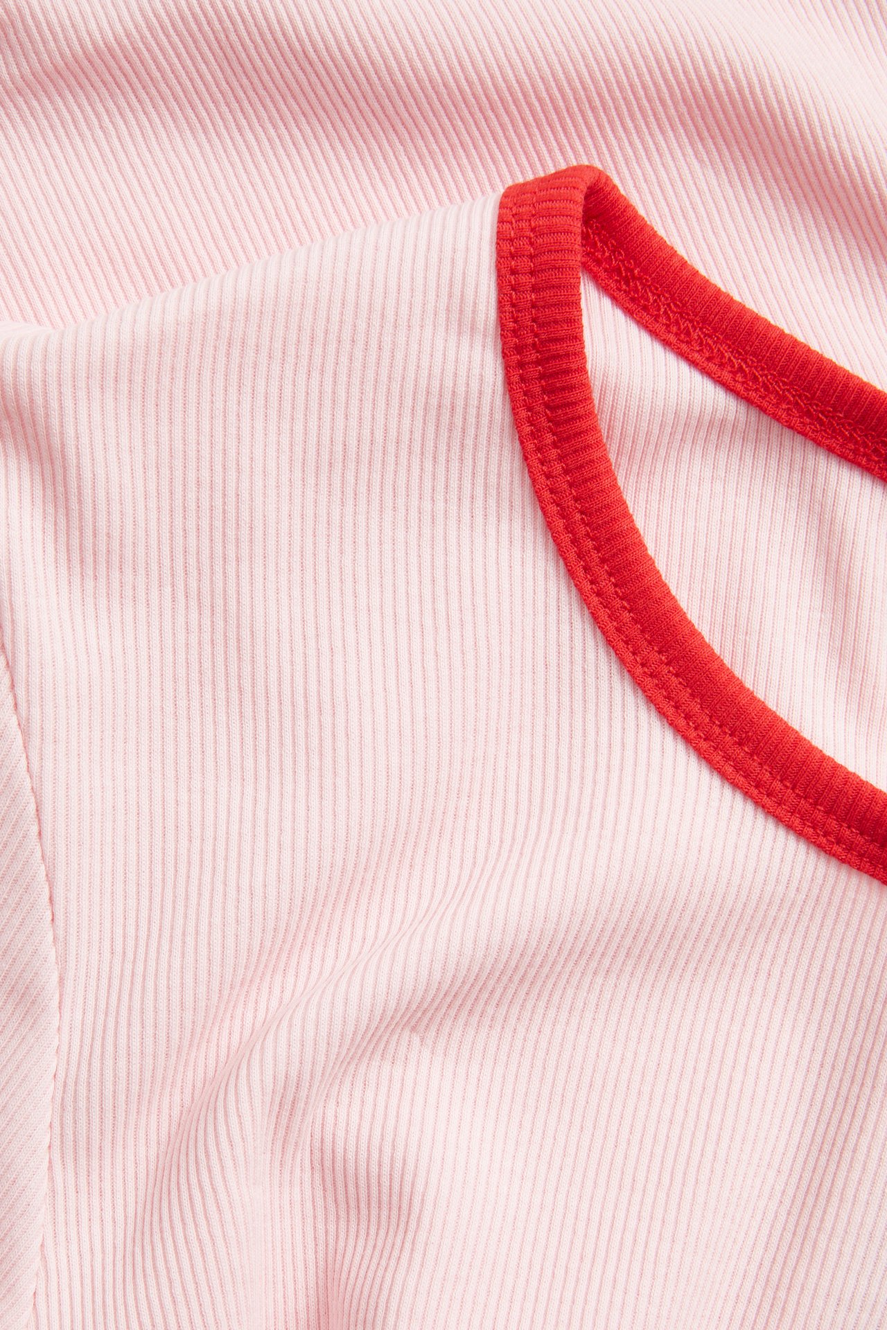 Nærbilde av en rosa ribbet baby-T-skjorte med rød kontrasterende halskant.