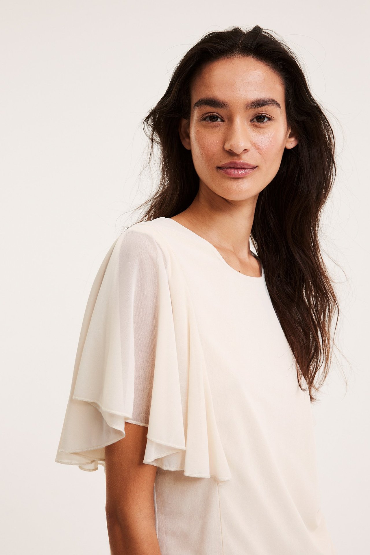 Framifrån på kvinna i offwhite skir topp med korta, vida ängelsärmar.