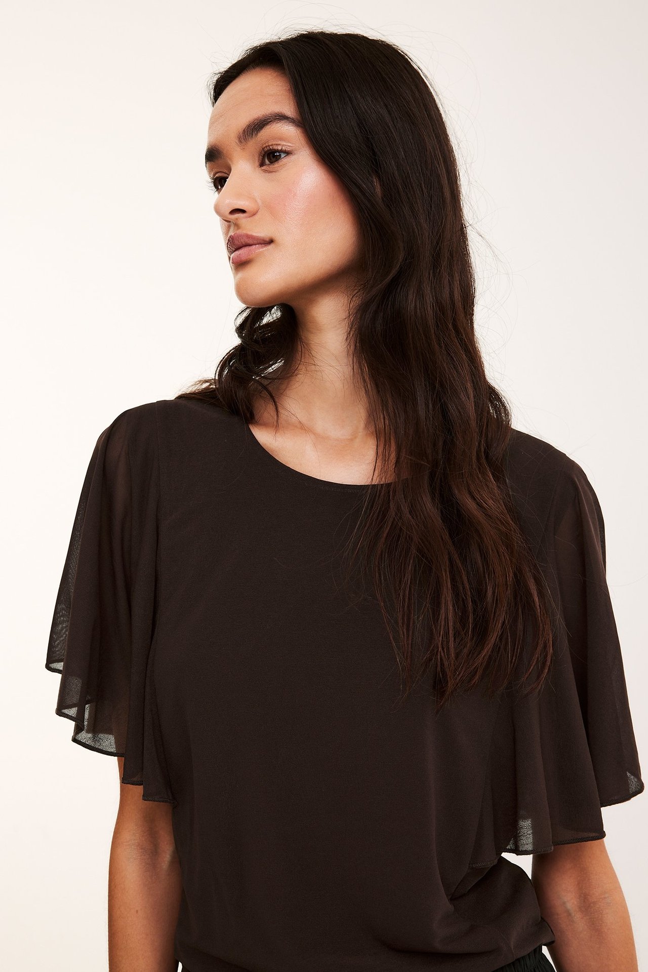 Nærbilde, front av kvinne i en mørkebrun gjennomsiktig topp med rund hals og vide korte ermer.