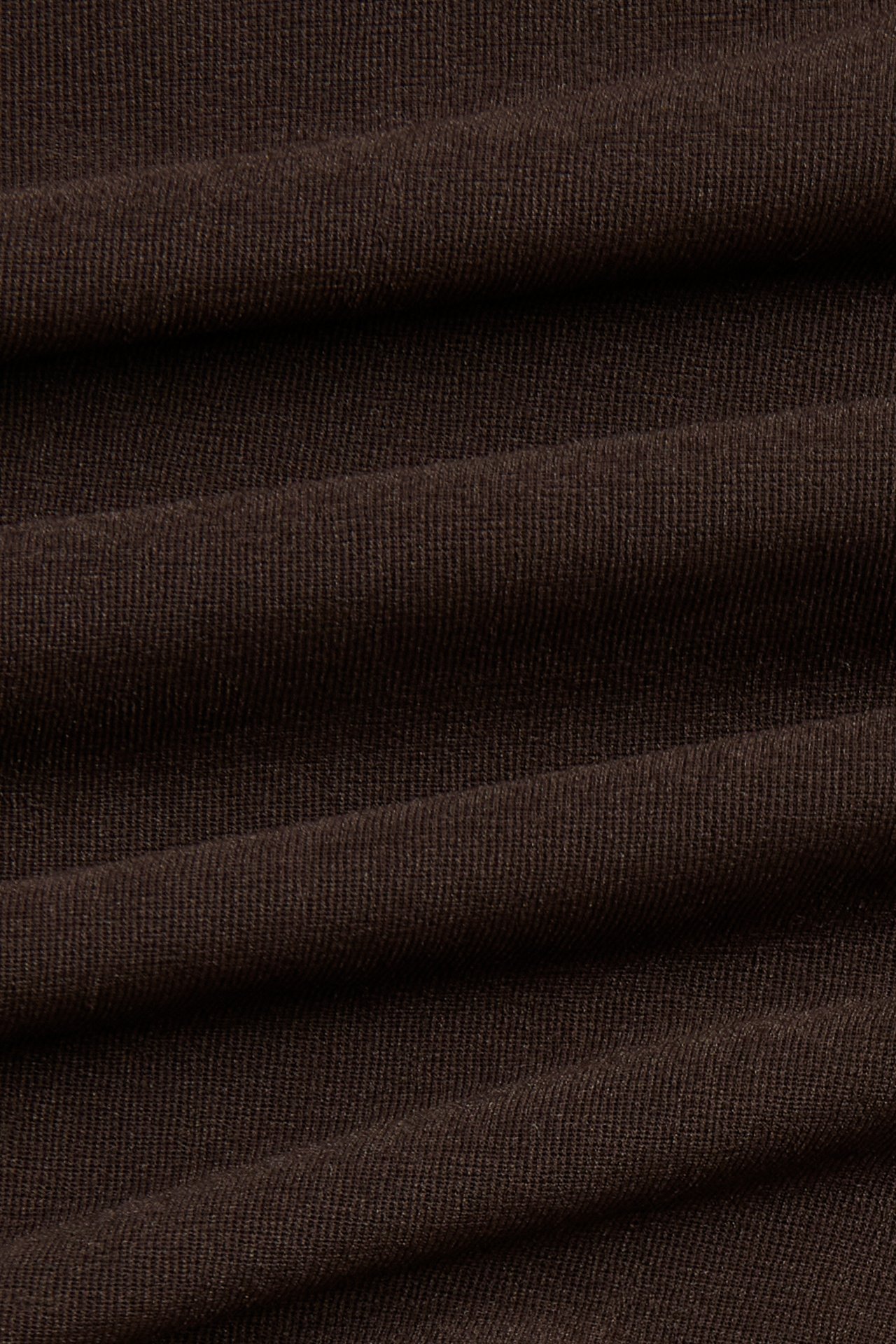 Närbild av det mörkbruna, enfärgade tyget till en tunn topp, med en subtil ribbad textur.
