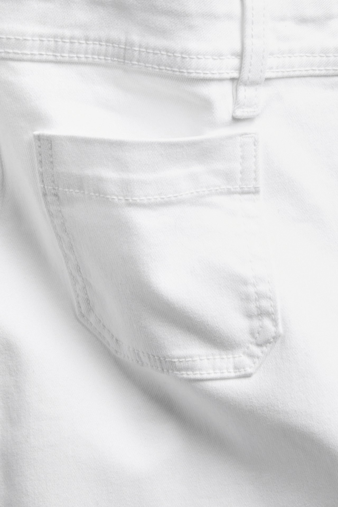 Närbild av vit twillshorts bakficka, med synliga sömmar och en hällare.