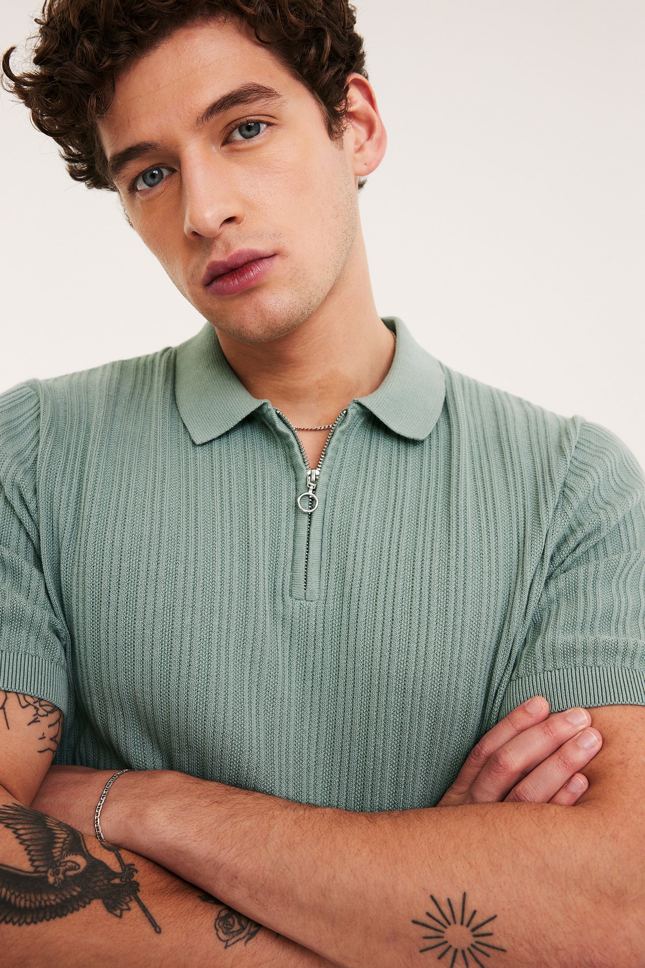Jasnozielona prążkowana dzianinowa koszulka polo z zamkiem, na mężczyźnie, widok z przodu, z łańcuszkiem.