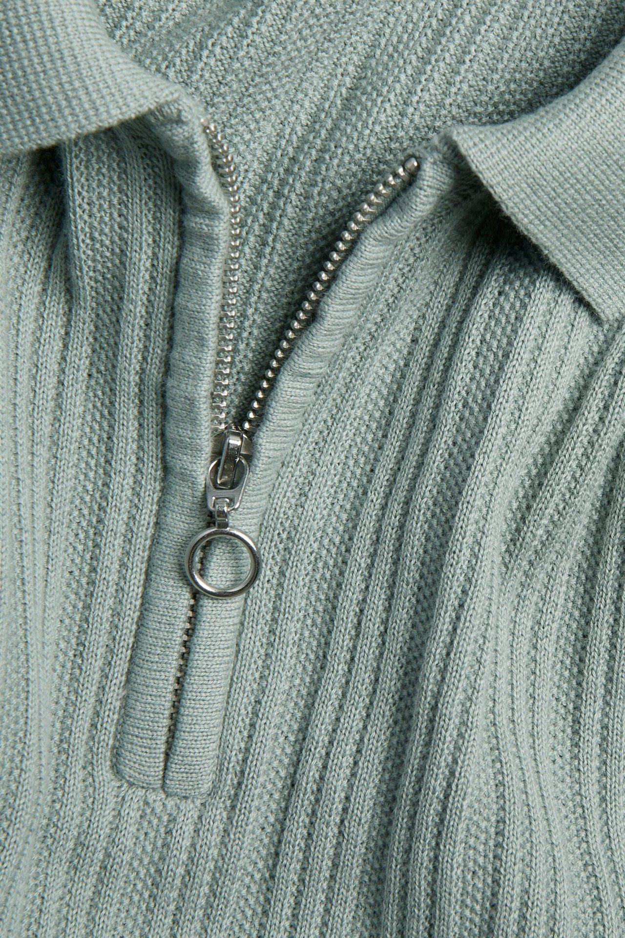 Nærbilde av en lysegrønn strikket half-zip pikétrøye med strukturmønster.