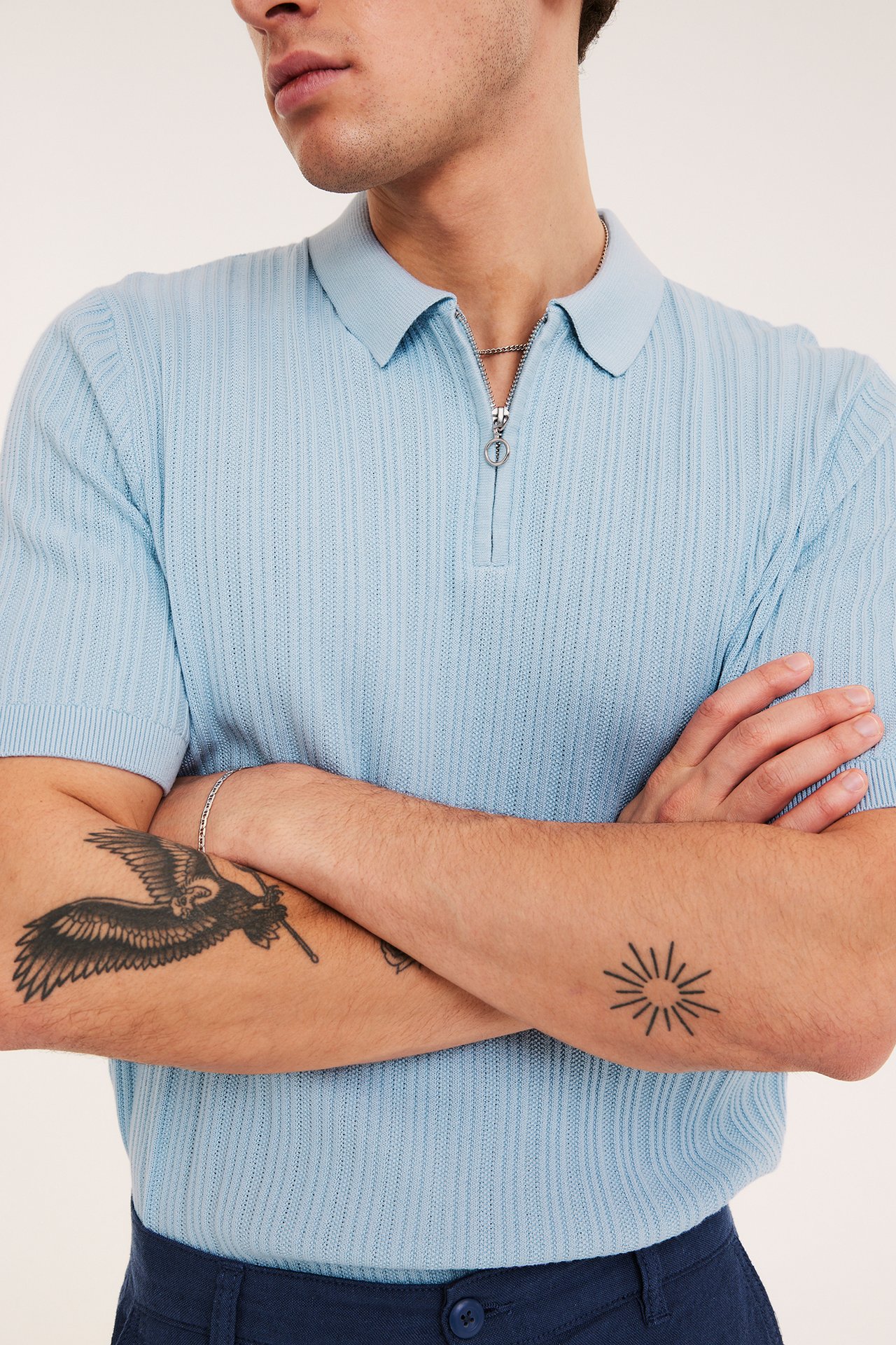 Mężczyzna w jasnoniebieskiej dzianinowej koszulce polo z suwakiem, granatowych spodniach, z przodu.