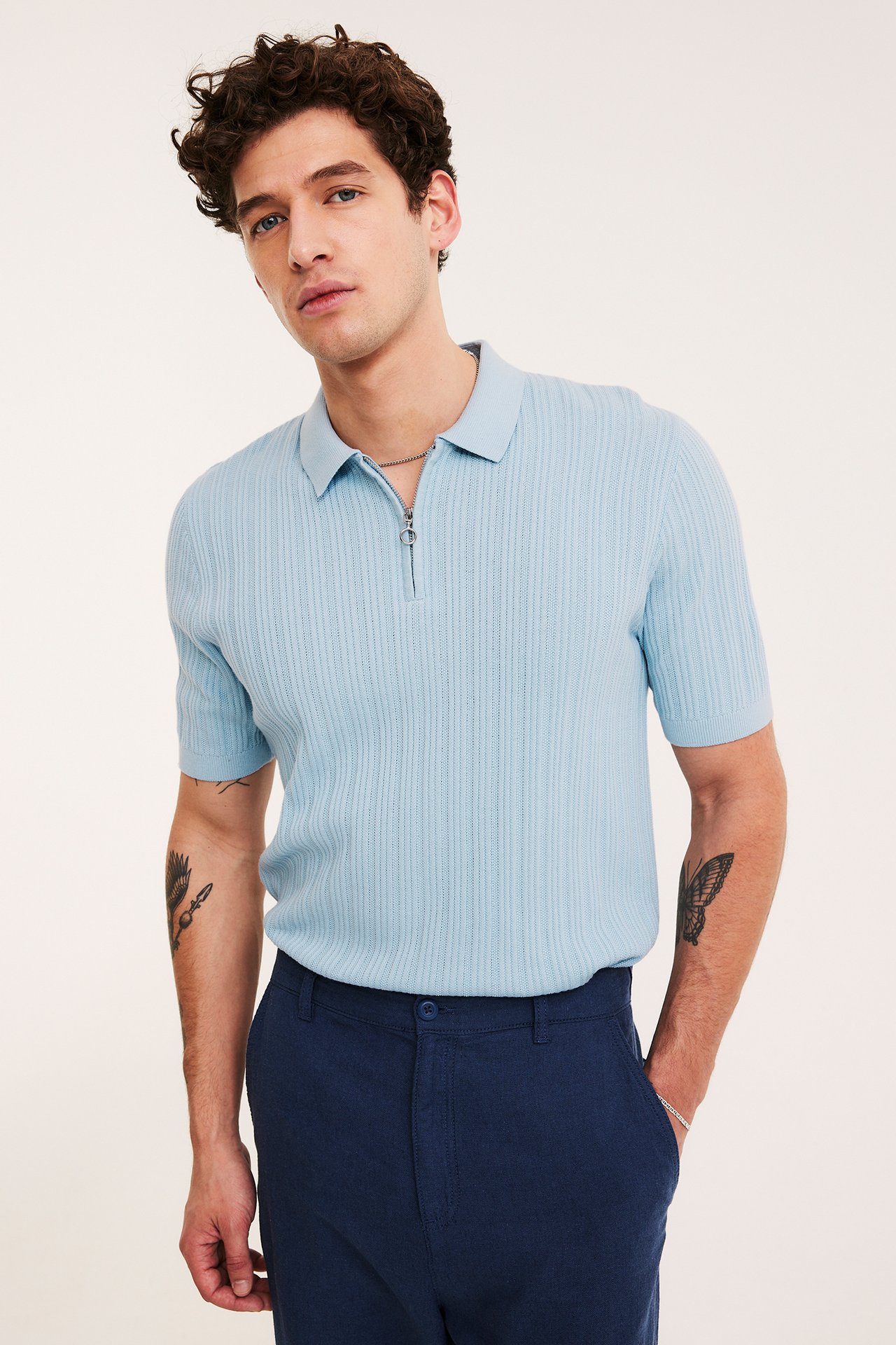 Widok z przodu: mężczyzna w jasnoniebieskiej prążkowanej koszulce polo half-zip i granatowych spodniach.