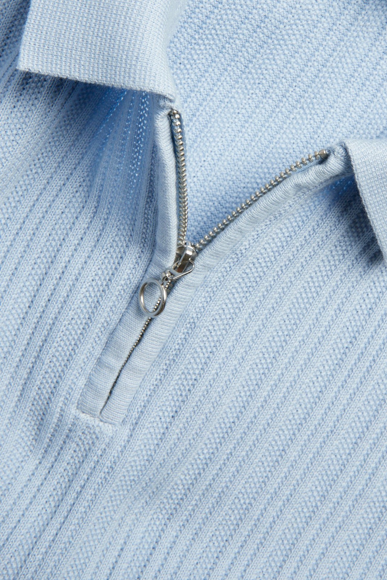 Zbliżenie na jasnoniebieską dzianinową koszulkę polo ze srebrnym zamkiem half-zip i wzorem strukturalnym.