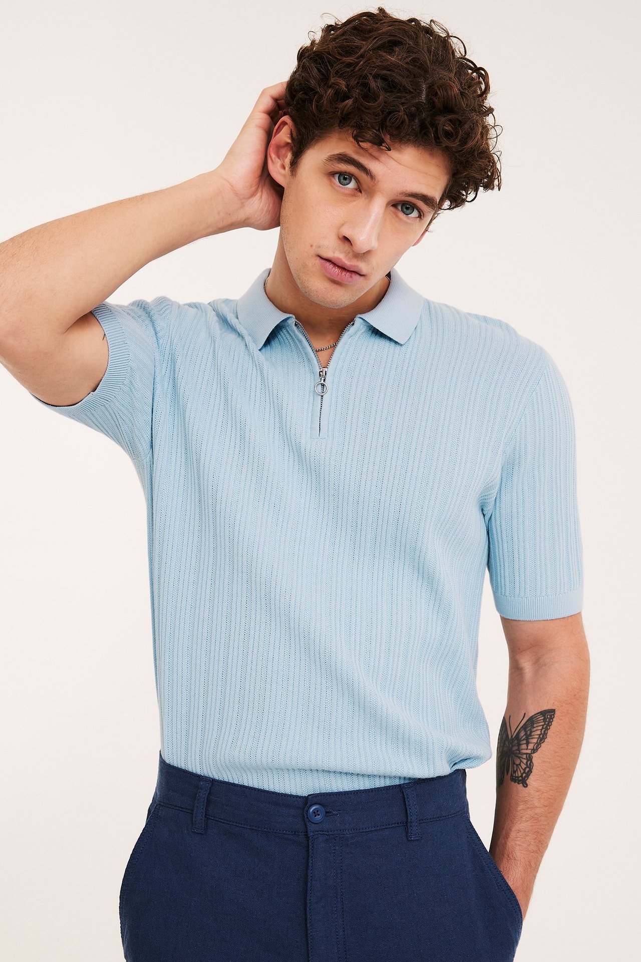 Mężczyzna w jasnoniebieskiej dzianinowej koszulce polo half-zip i granatowych spodniach.