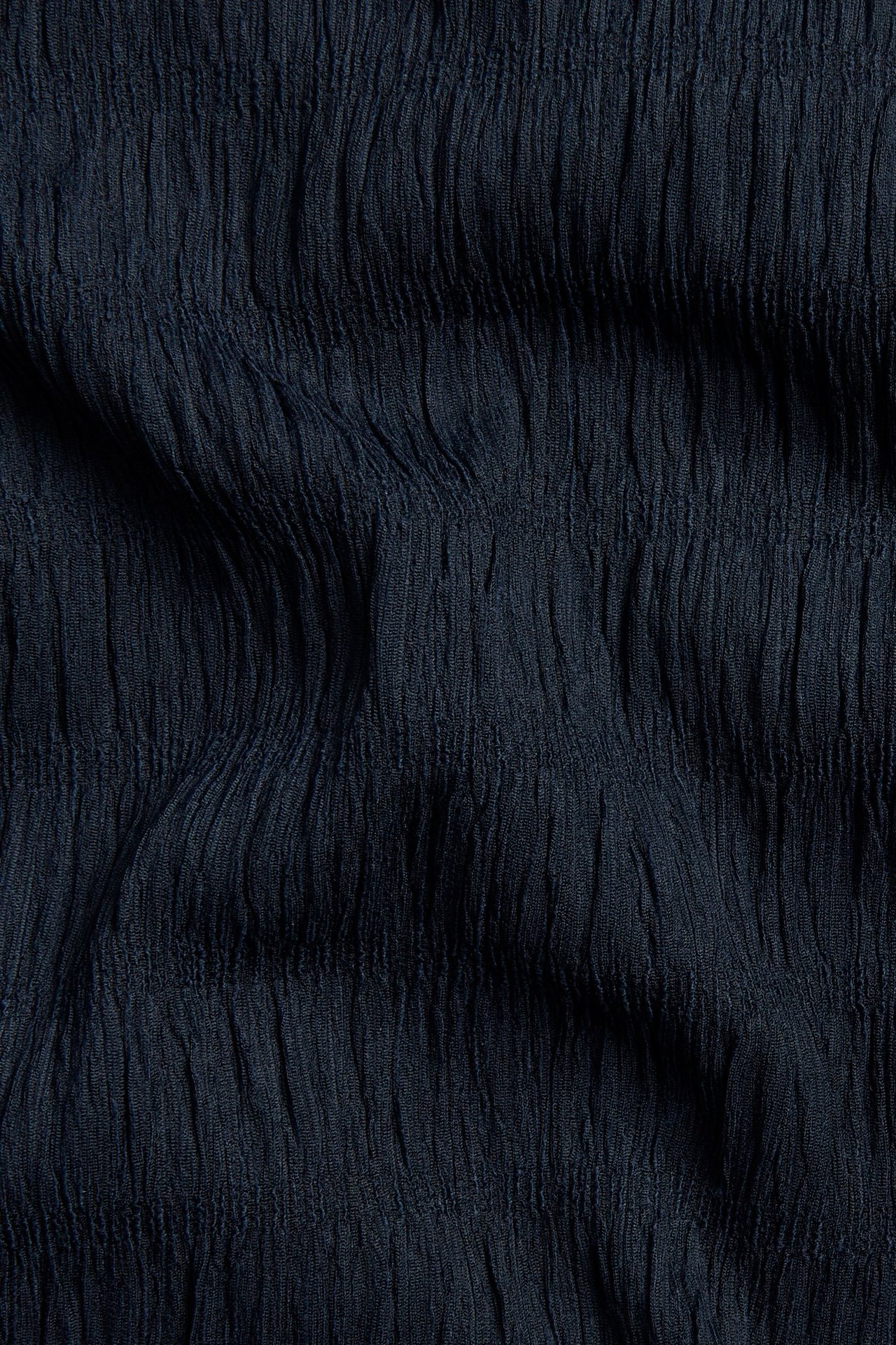 Lähikuva tummansinisestä kuvioidusta kankaasta lyhythihaisesta peplum-topista.