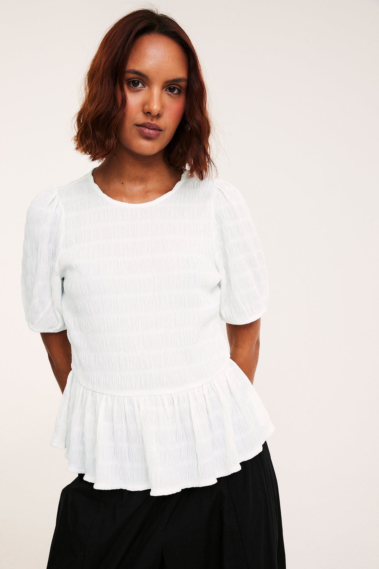 Frontutsikt, kvinne i offwhite strukturert peplumtopp med puffermer og svarte underdeler.