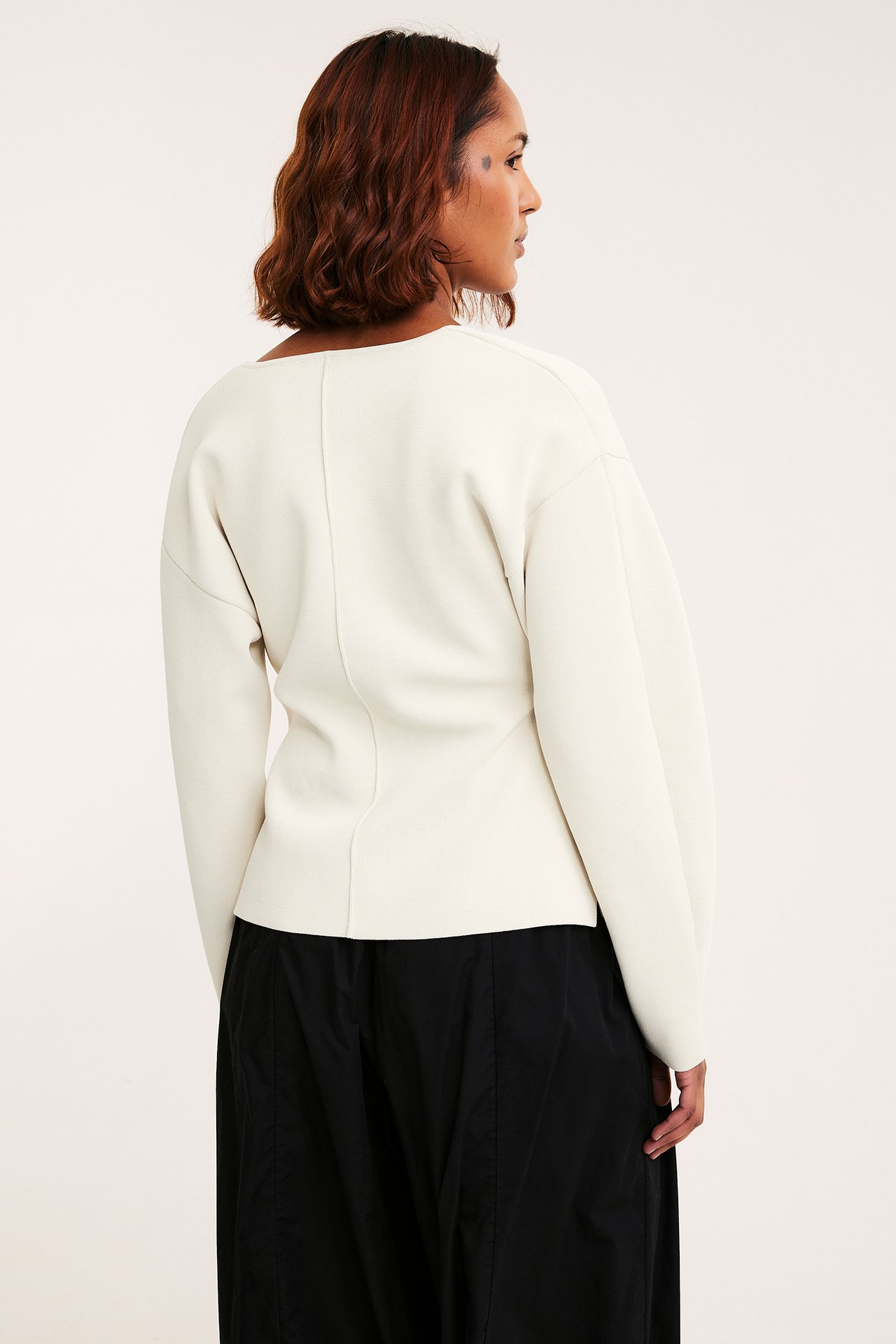 Sido-bakvy av kvinna i offwhite figursydd långärmad kofta och svarta byxor.