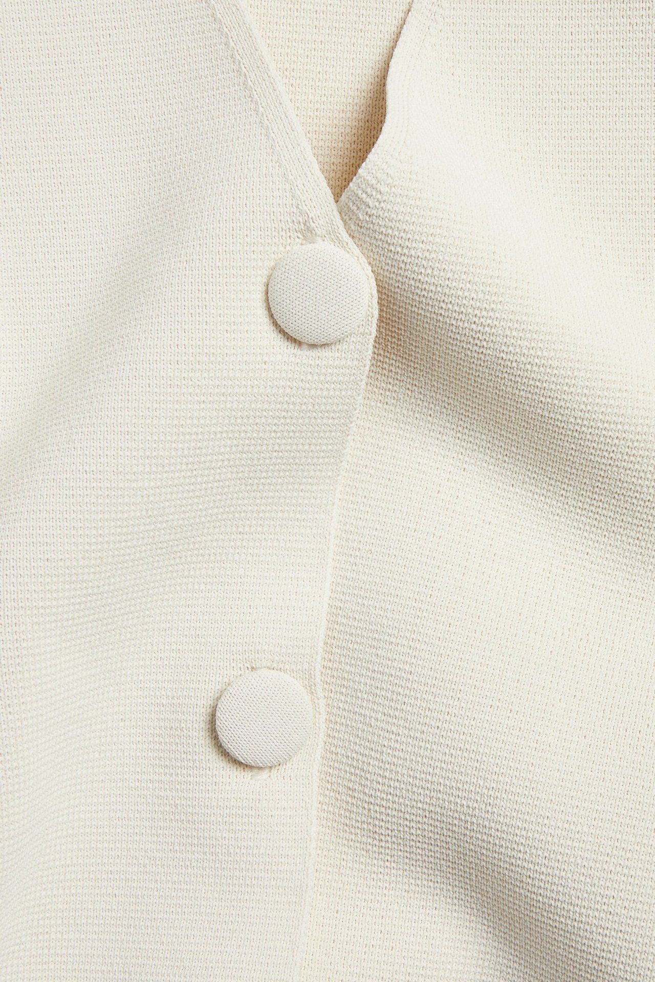 Nærbilde av en ensfarget offwhite cardigan i polyesterblanding med to stoffdekkede knapper foran.
