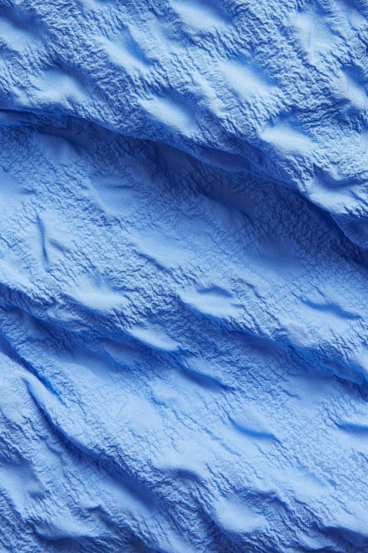 Närbild av klänningens blå strukturerade tyg, som visar dess skrynkliga yta.