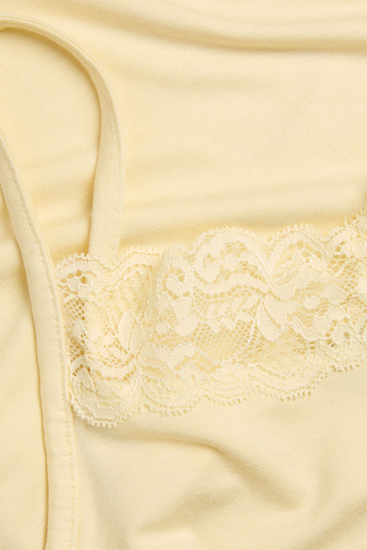 Närbild av ett ljusgult linne med delikat ljusgul spetskant längs överkanten.