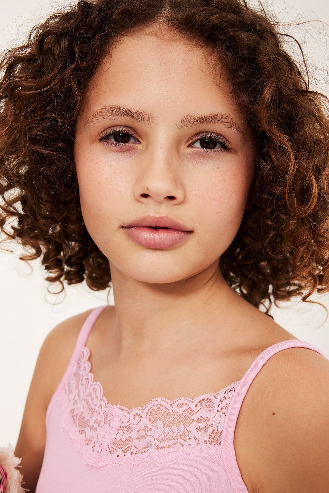 Lähikuva edestä lapsesta, joka käyttää vaaleanpunaista pitsireunustettua toppia.