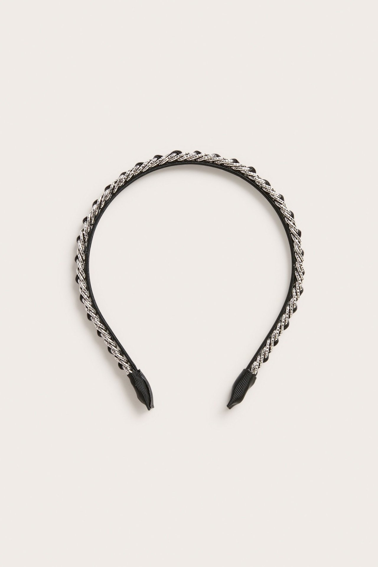 Flat lay av et svart diadem i fløyel med flettet sølvfarget metalldetalj.