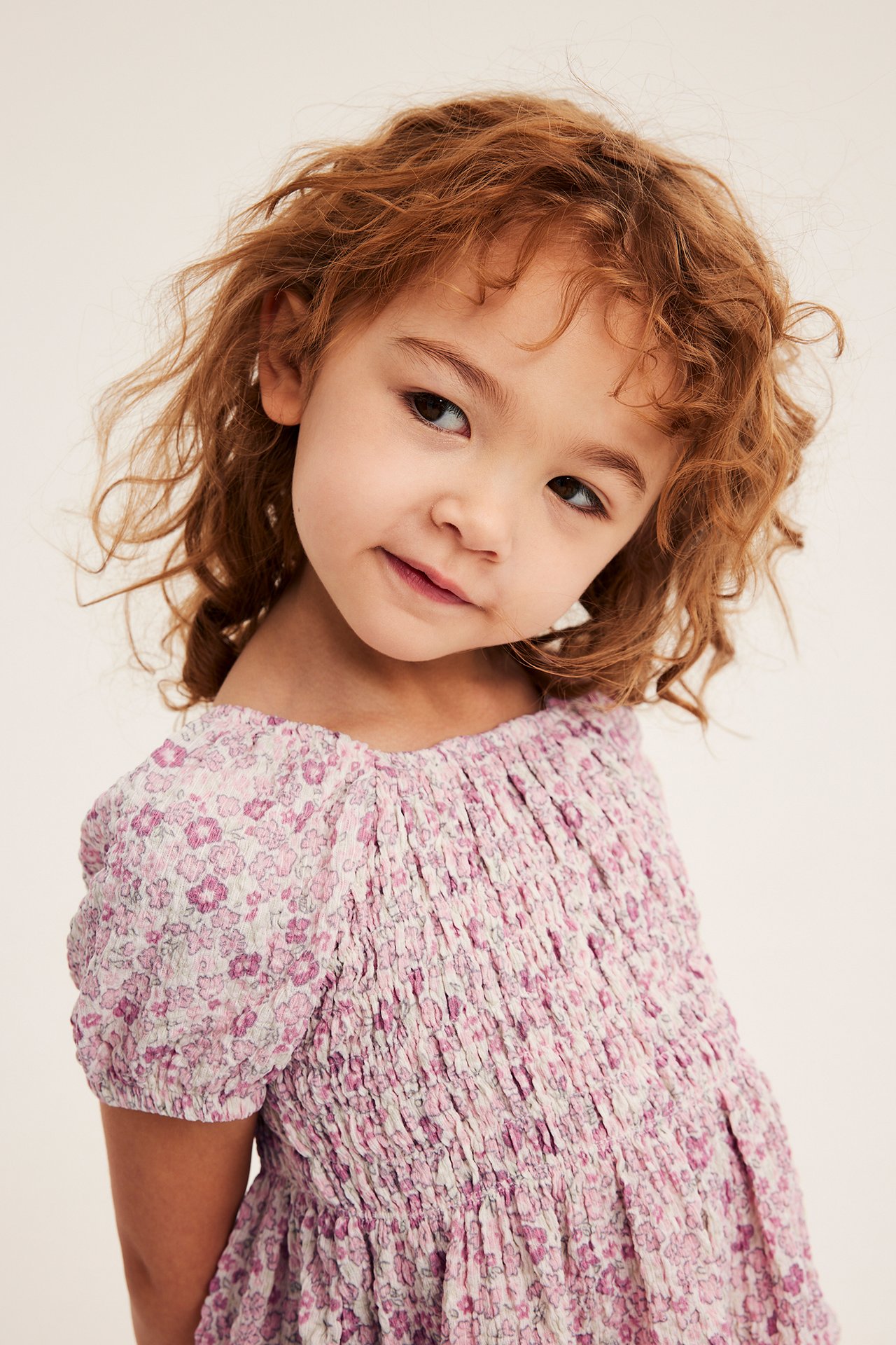 Från framsidan: ett barn bär en offwhite blommig smocktopp med puffärmar.