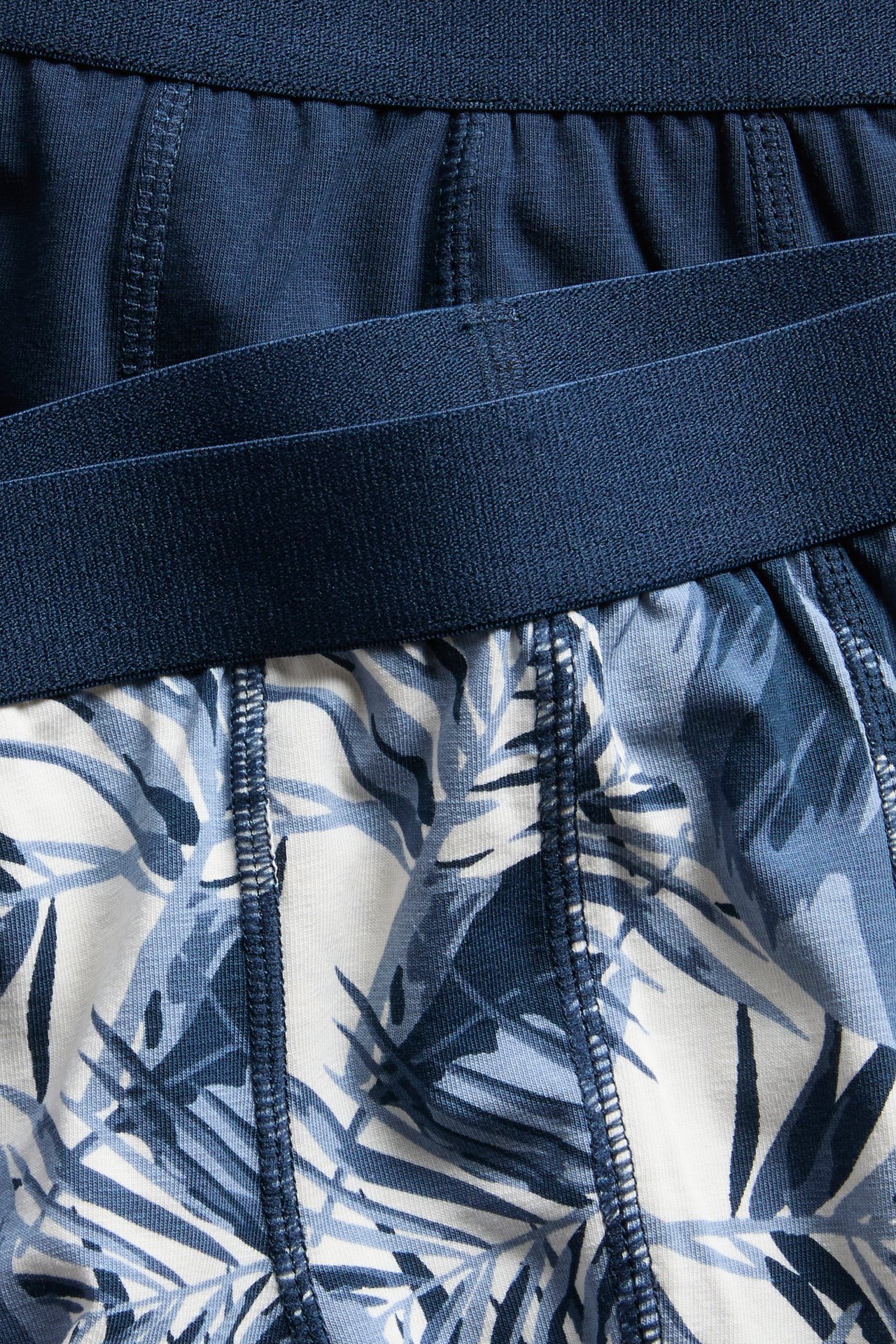 Närbild uppifrån på två kalsonger för barn: en enfärgad mörkblå, en vit med blått bladmönster i bomull.