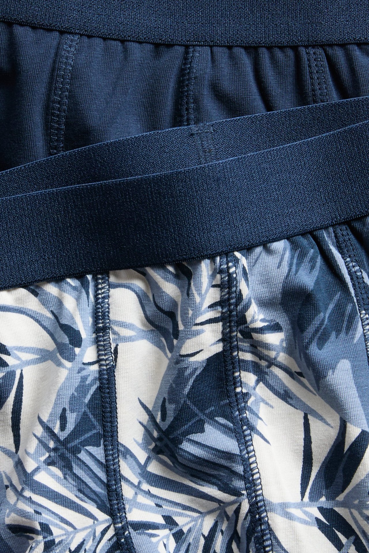 Lähikuva kahdesta lasten puuvillabokserista: yksi yksivärinen laivastonsininen, toinen luonnonvalkoinen sinisellä lehtikuviolla.