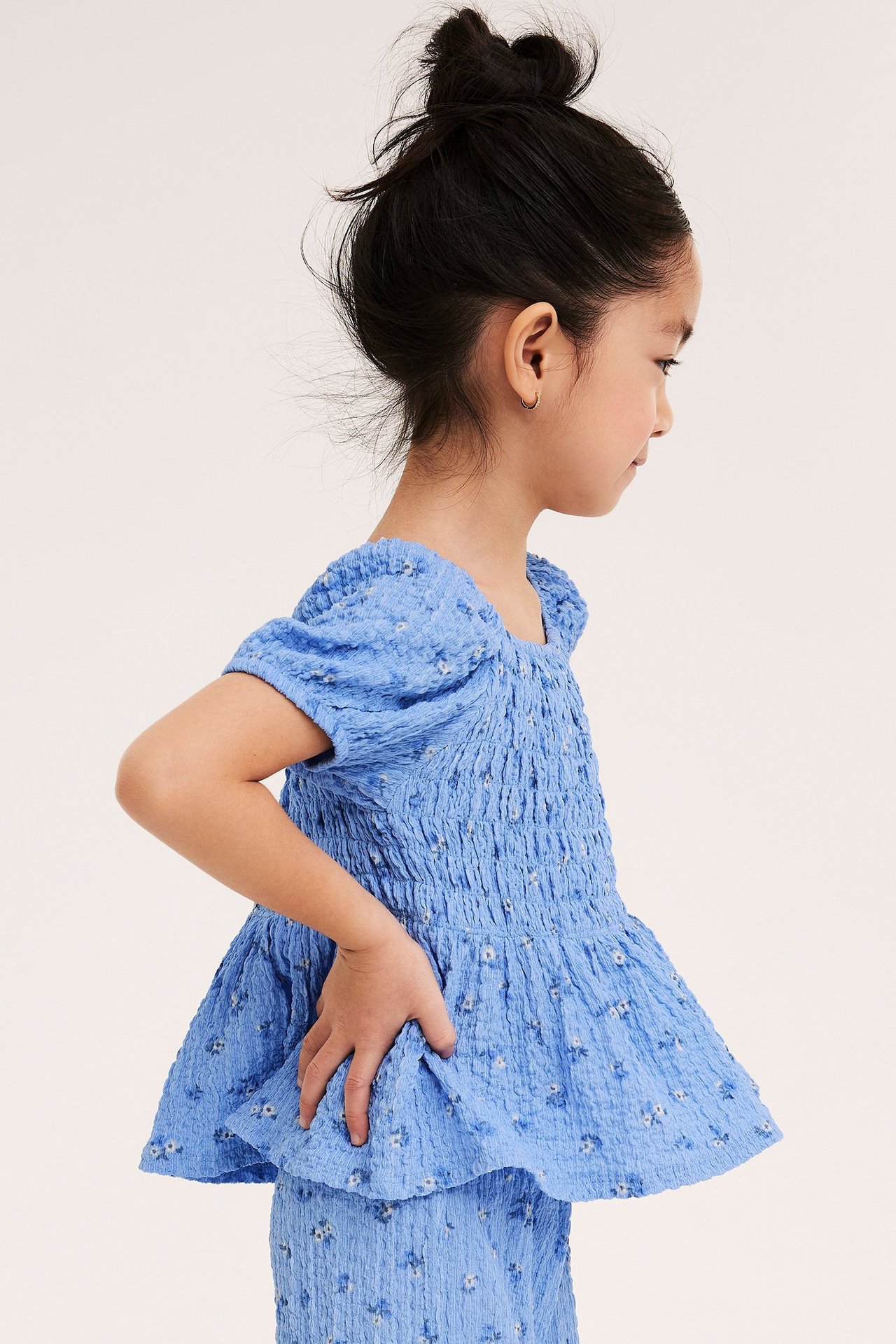 Sidovy av ett barn i en ljusblå blommig smocktopp med puffärmar och matchande culottes.