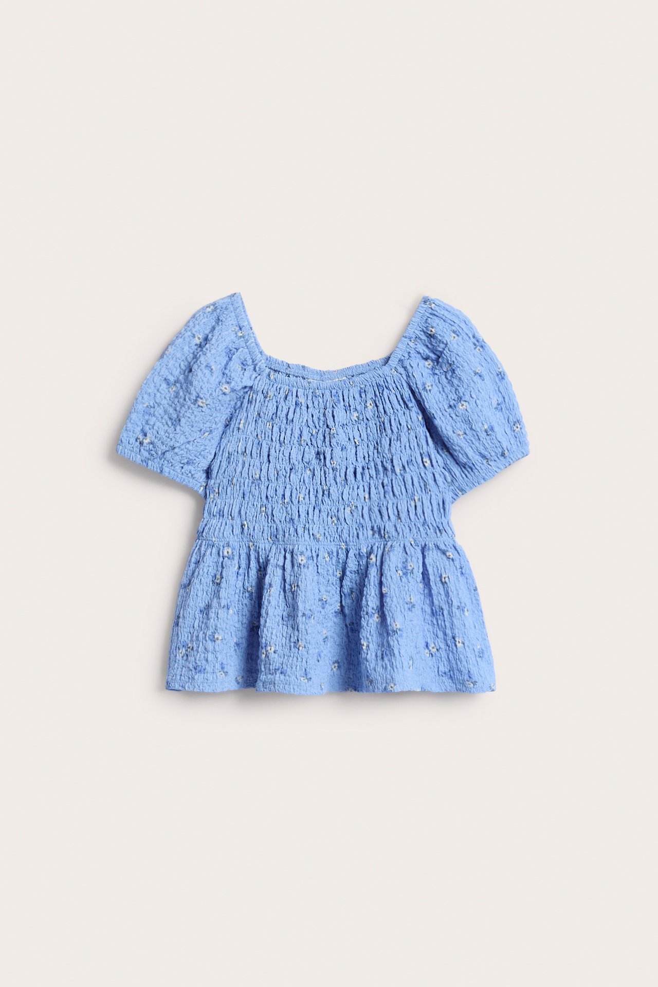 Przód jasnoniebieskiego topu ze strukturalnej dzianiny ze smockiem, kwiatowym wzorem i bufiastymi rękawami.
