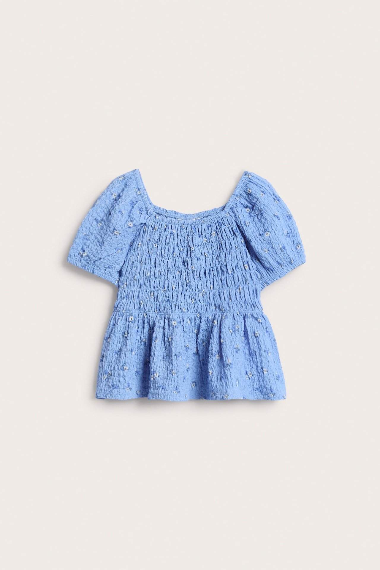 Framsida av en ljusblå topp i strukturerad trikå med smock, blommigt mönster och puffärmar.