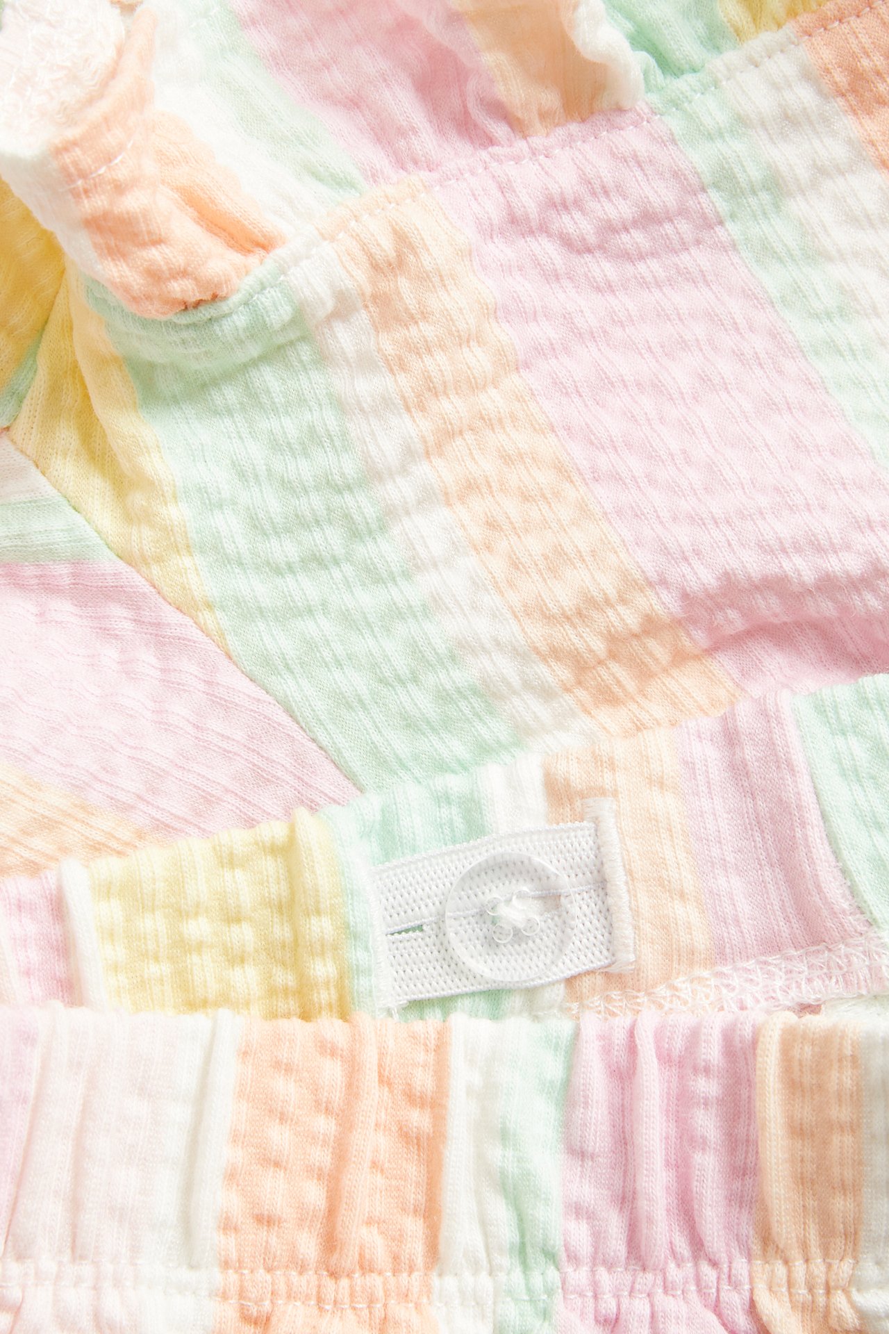 Närbild av barnshorts i mjuk, strukturerad flerfärgad bomullstrikå med volangkant och justerbar midjeknapp.