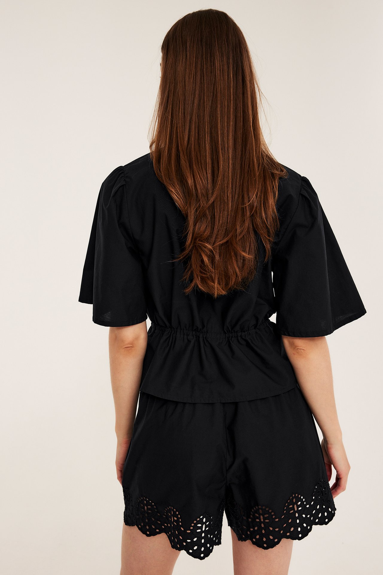 Ryggvy av kvinna i svarta shorts i bomullspoplin med broderie anglaise och matchande svart topp.