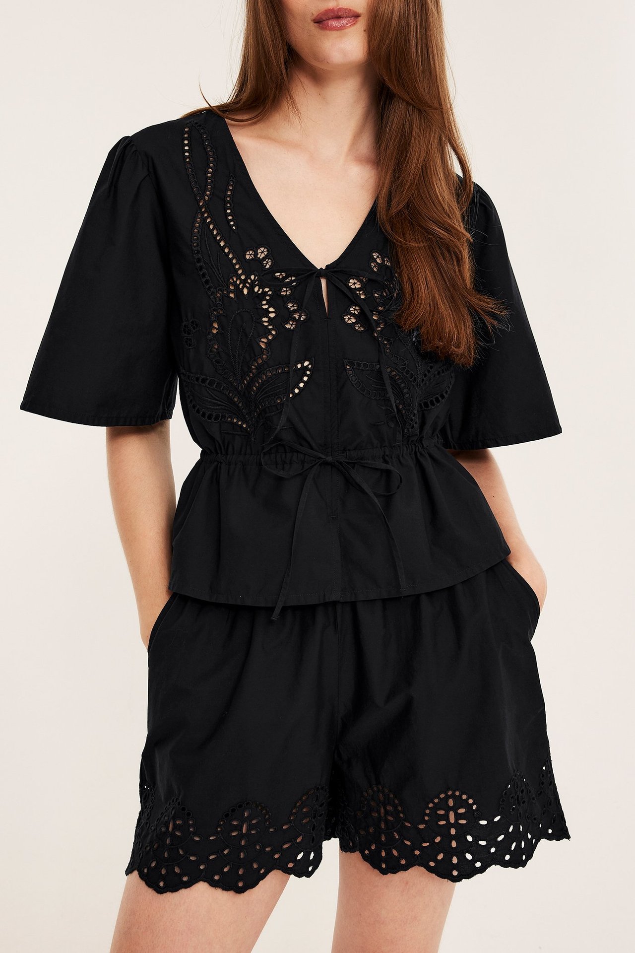 Edestä päin, nainen mustissa puuvillapopliinishortseissa, joissa broderie anglaise, yhdessä mustan kirjaillun puseron kanssa.