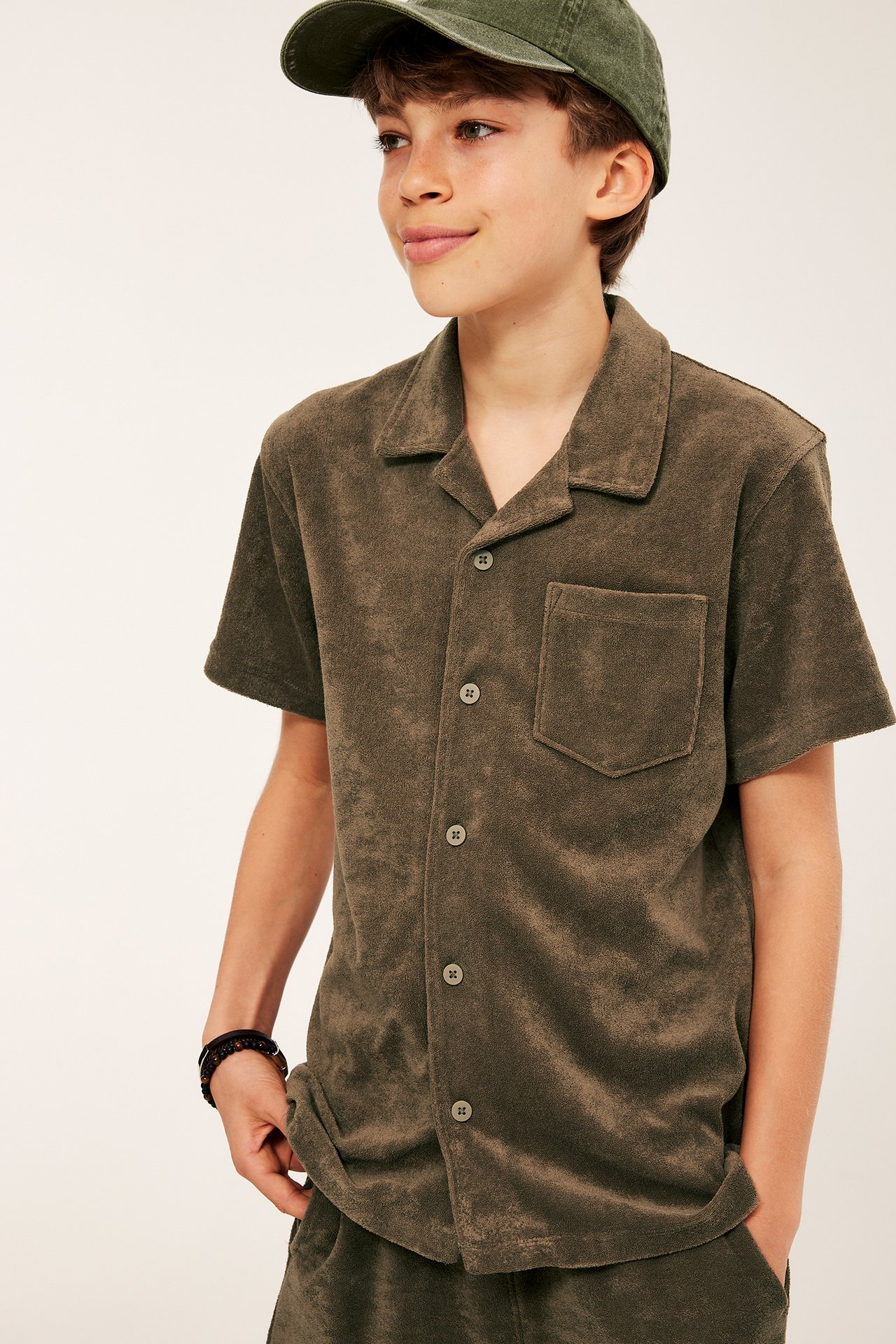 Widok z przodu: chłopiec w khakibrązowej koszuli frotte, pasujących szortach i czapce.