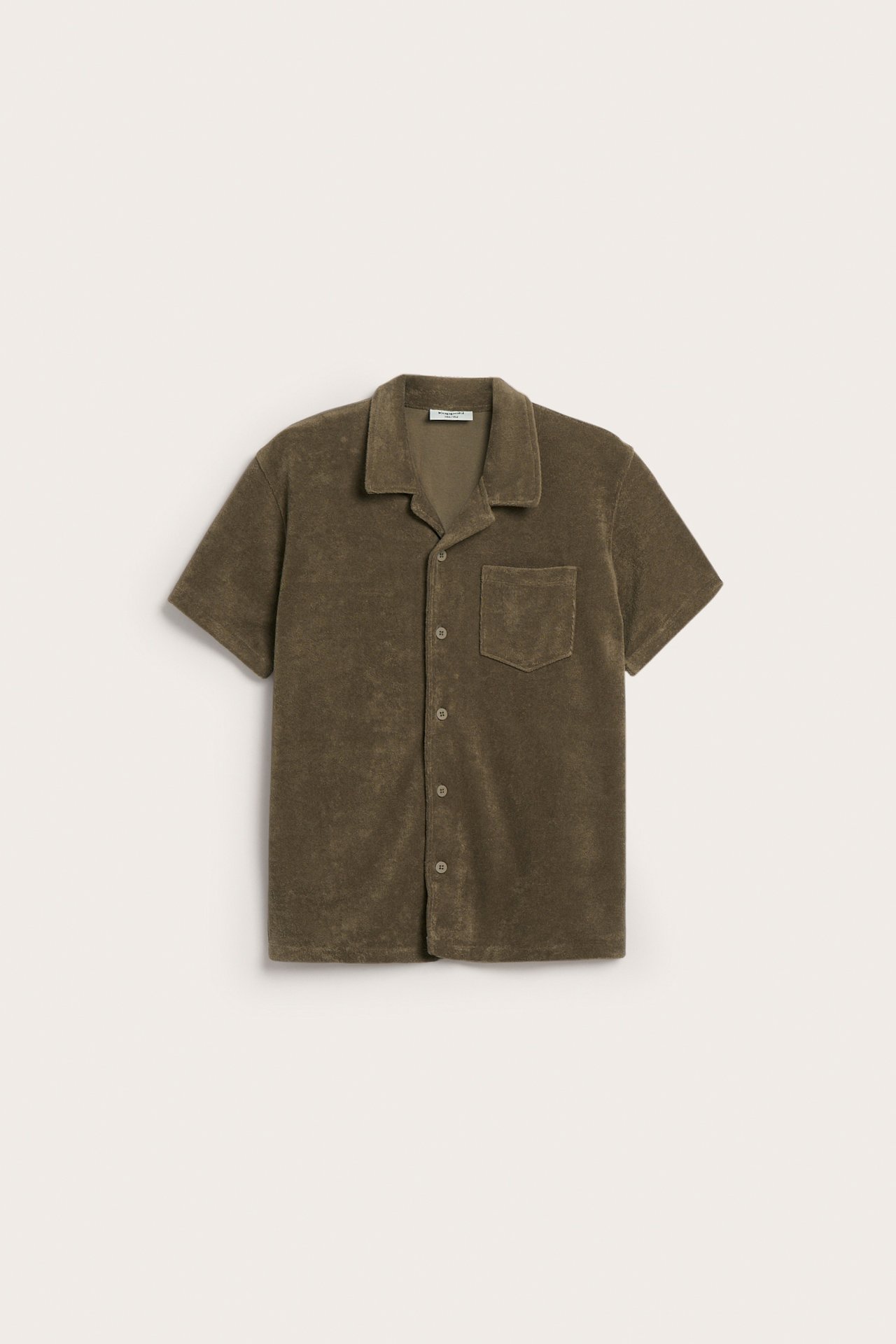 Framifrån, en brun kortärmad frottéskjorta med resortkrage, bröstficka och knappar fram.