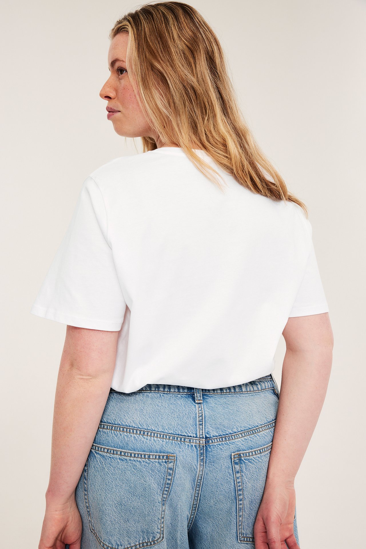 Naisen takakuva valkoisessa puuvilla T-paidassa ja vaaleansinisissä farkuissa.