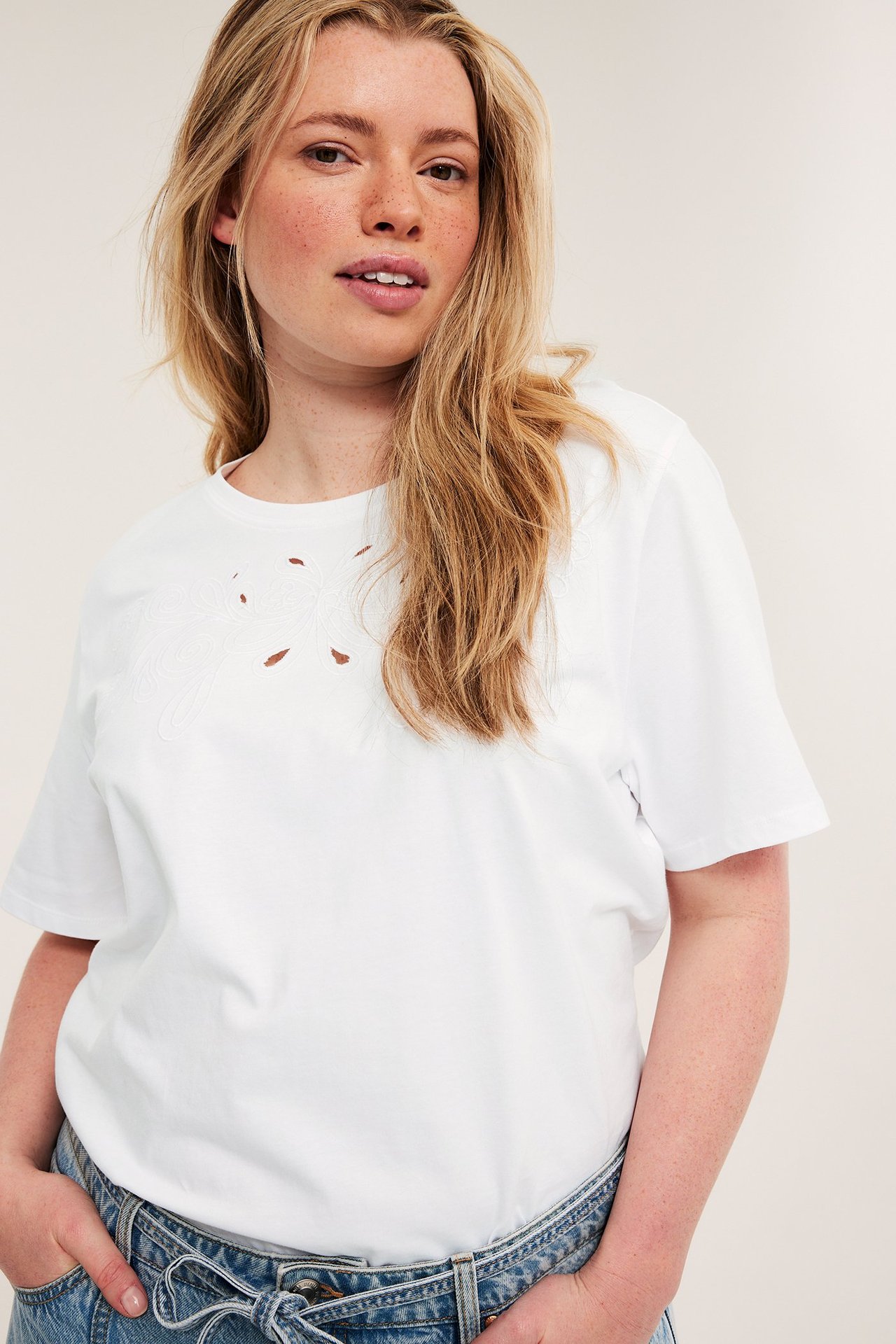 Närbild framifrån på kvinna i vit bomulls-t-shirt med broderie anglaise och blå jeans.