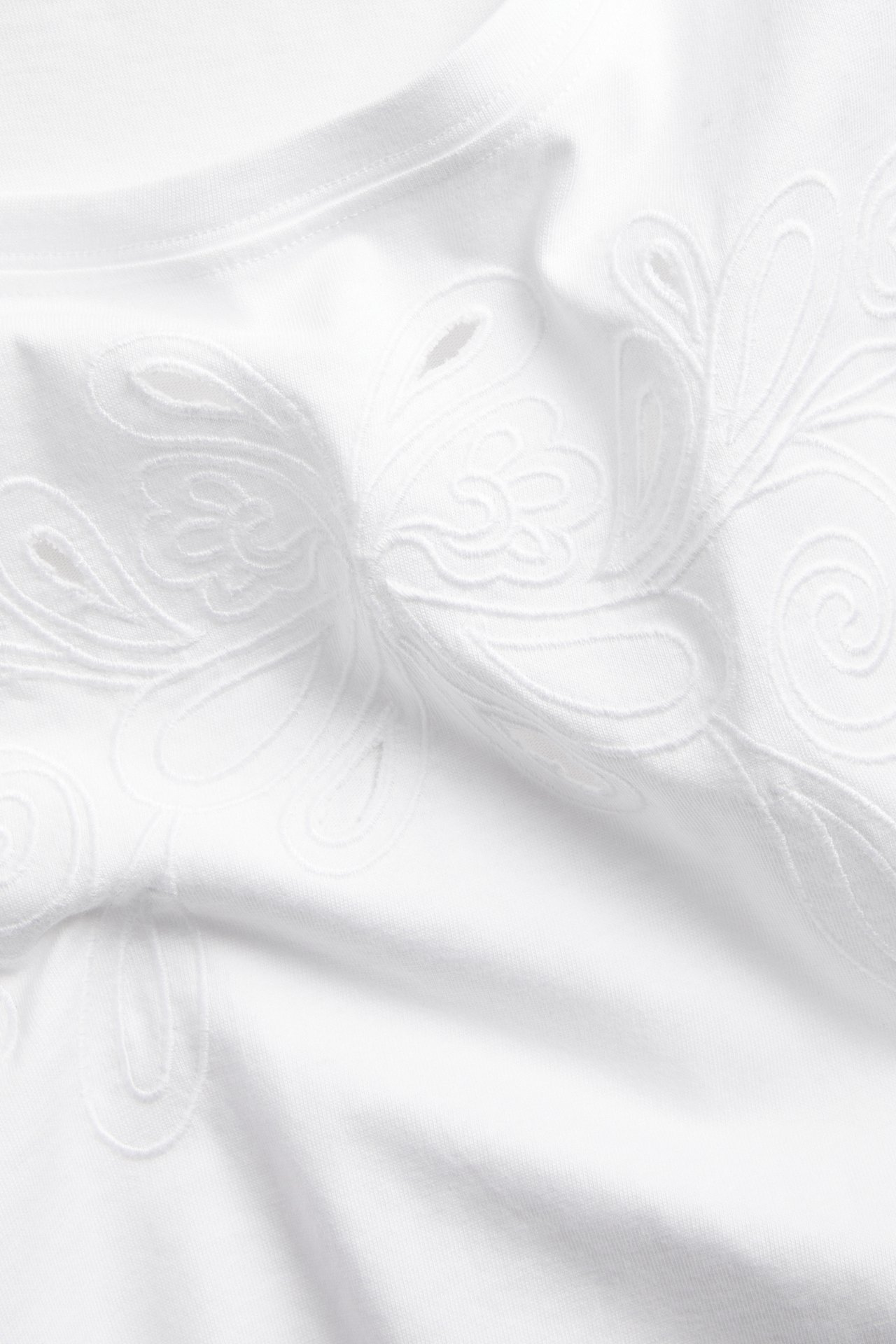 Nærbilde av en hvit bomulls-T-skjorte med detaljert broderie anglaise-broderi.