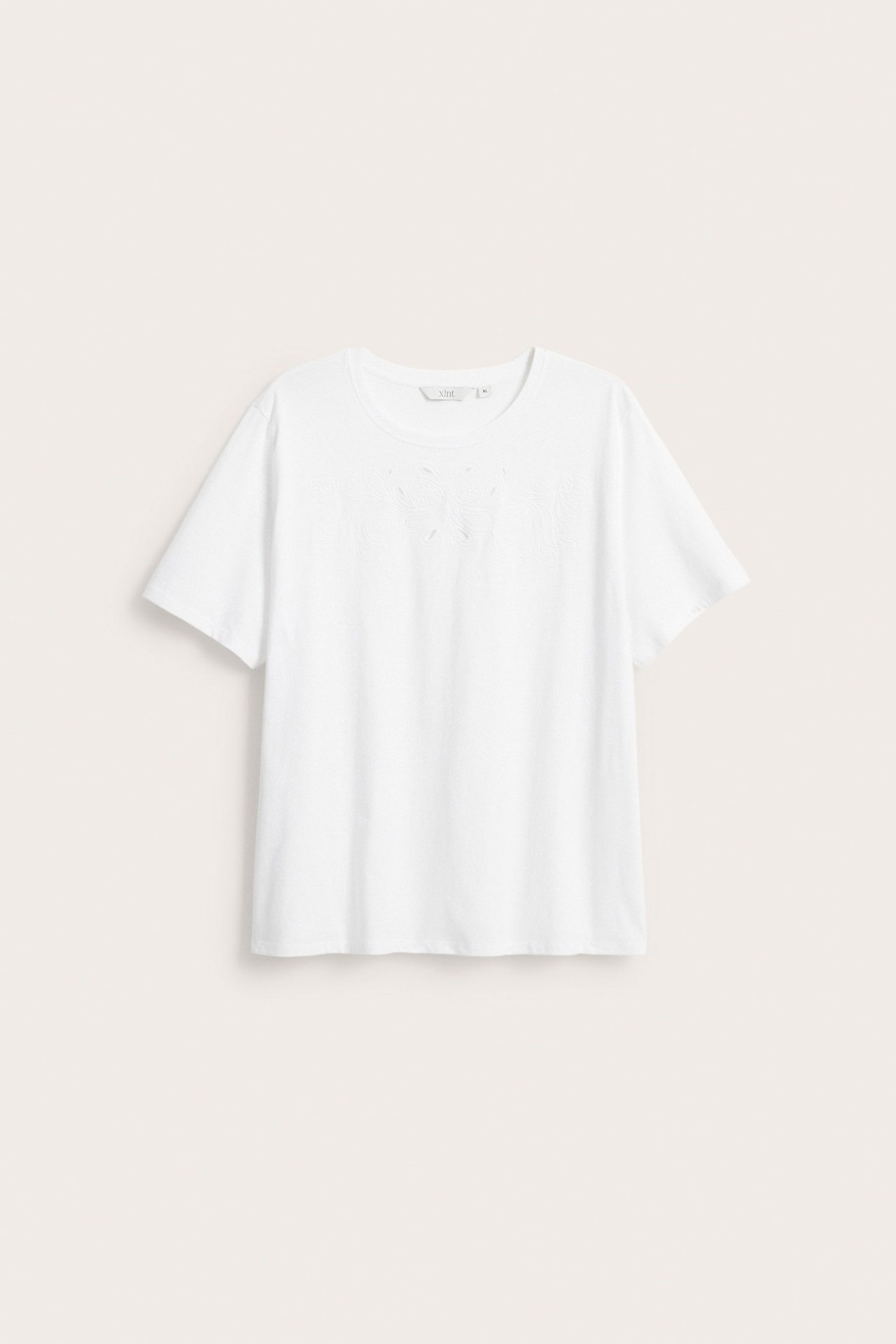 Edestäpäin valkoinen puuvillainen t-paita lyhyillä hihoilla ja broderie anglaise -kuviolla rinnassa.