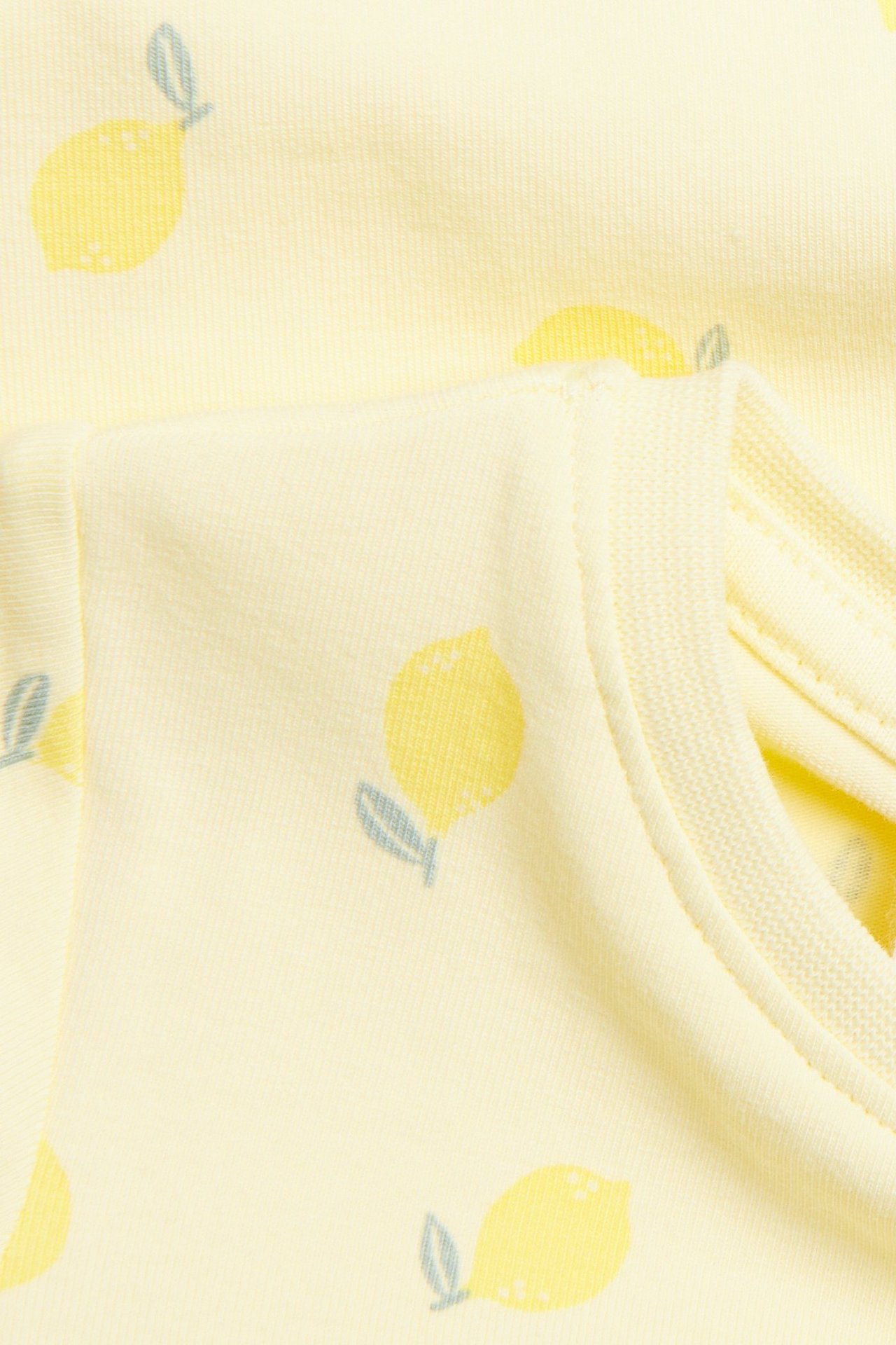 Närbild på en ljusgul kortärmad babybody i single jersey med citronmönster.