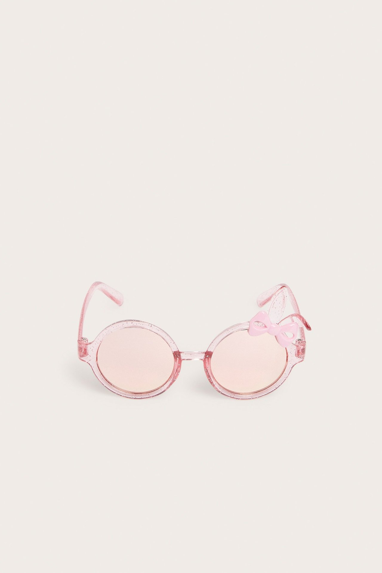 Frontvy av glittriga ljusrosa runda barnsolglasögon med en liten rosa rosett och örondetalj.
