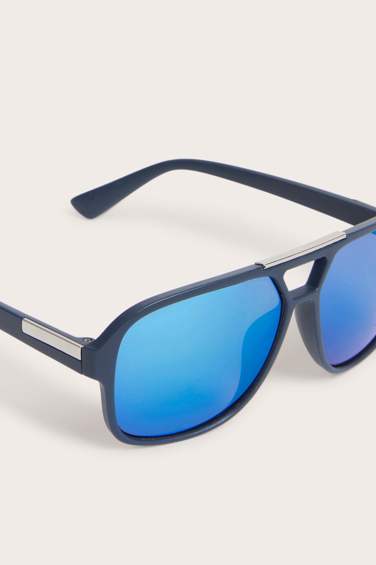 Zbliżenie na ciemnoniebieskie pilotki z jasnoniebieskimi lustrzanymi szkłami i srebrnymi detalami.