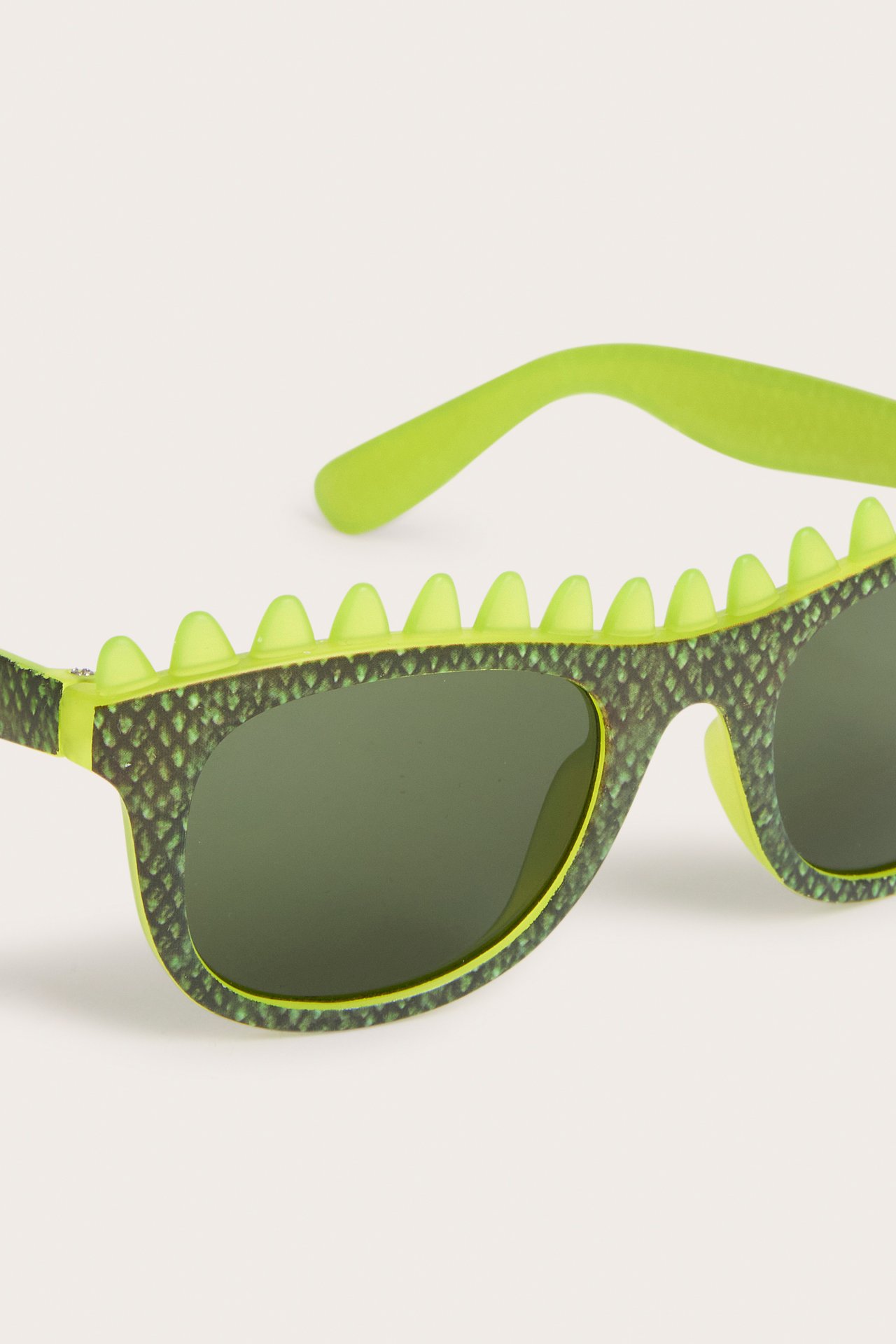 Zbliżenie jasnozielonych okularów przeciwsłonecznych dla dzieci ze wzorem łusek dinozaura i detalami grzbietu.