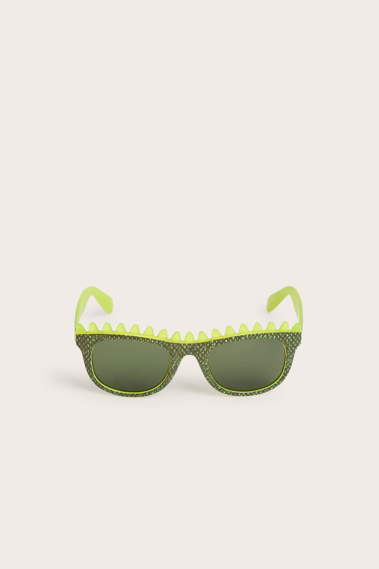 Widok z przodu jasnozielonych okularów przeciwsłonecznych dla dzieci z wzorem łusek dinozaura i kolcami.