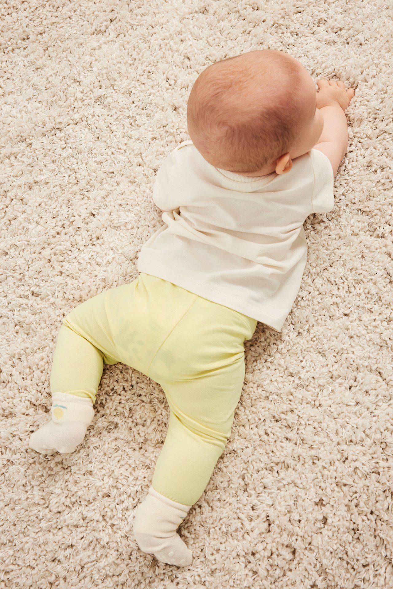 Widok z góry: dziecko w jasnożółtych legginsach z nadrukiem, kremowym t-shircie i skarpetach.
