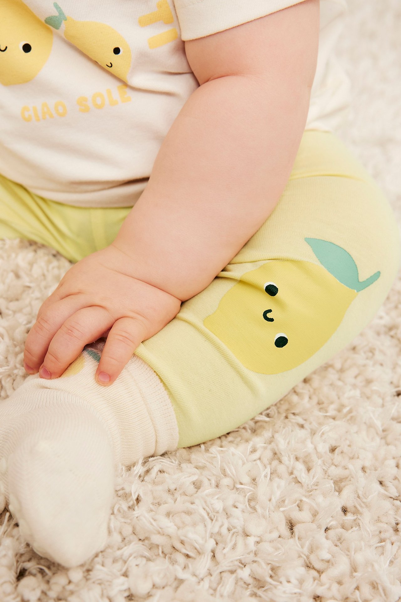 Nærbilde av en baby i lysegule leggings med sitronapplikasjoner, en kremfarget t-skjorte og kremsokker.
