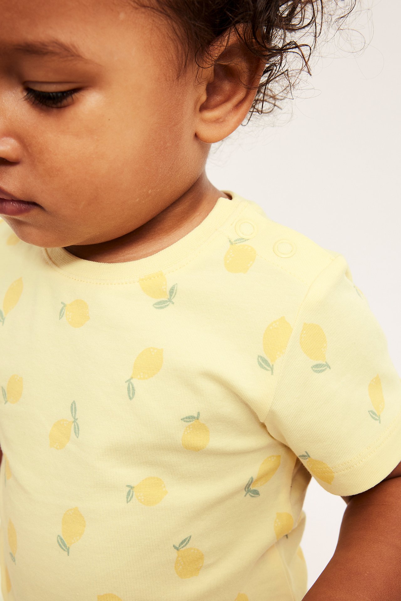 Zbliżenie na dziecko w jasnożółtej bluzce w cytryny, z zapięciem na napy na ramieniu.