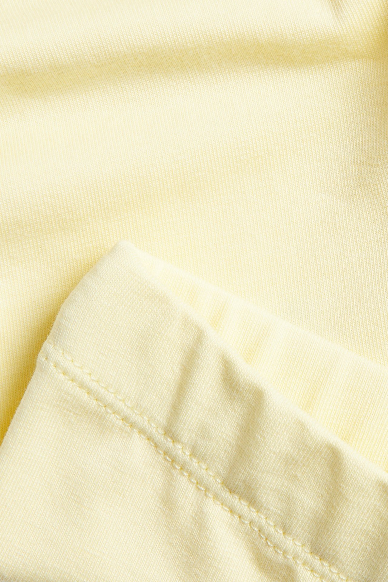 Närbild av ljusgul bomullsmix leggingsmaterial med ribbad textur och synlig söm.