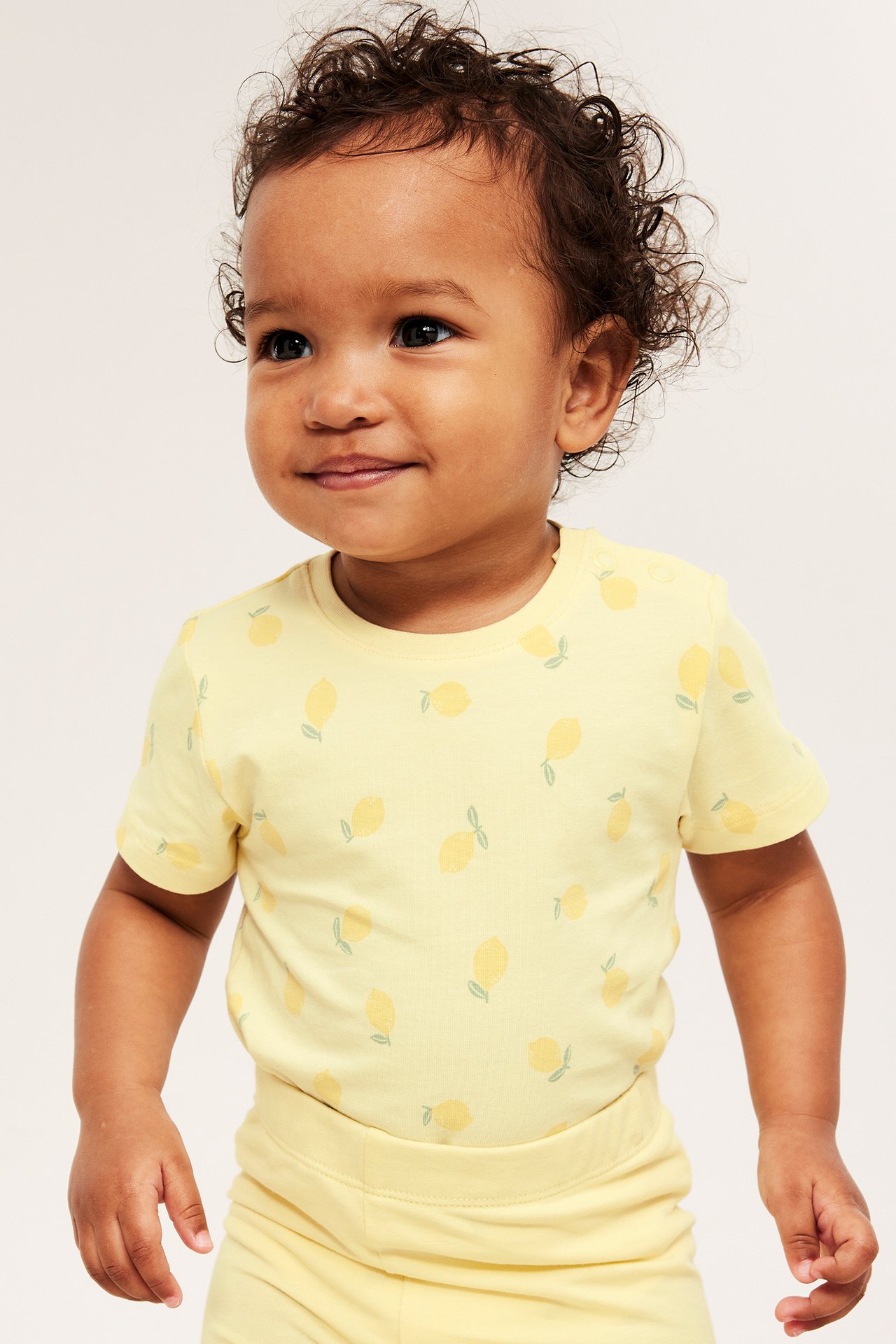 Baby i lysegule leggings med elastisk midje og matchende kortarmet topp med sitronmønster, forfra.